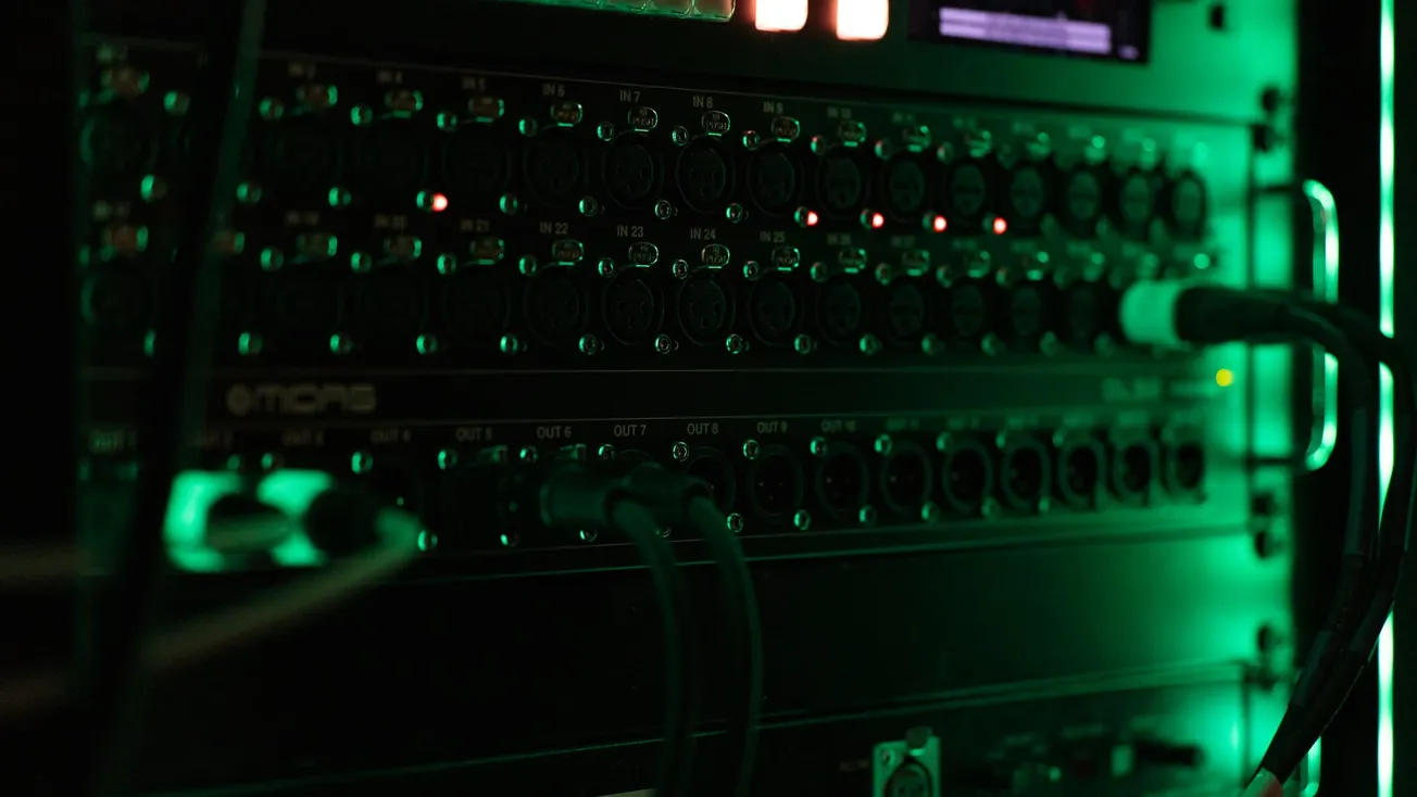 A dimly lit server rack with numerous black audio cables and glowing green lights, creating a high-tech and mysterious atmosphere.