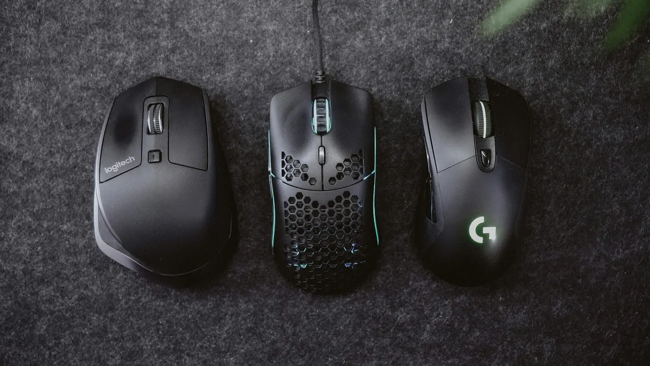 Three computer mice on a dark textured surface: a sleek black mouse, a perforated design mouse with glowing accents, and a mouse with a glowing logo.