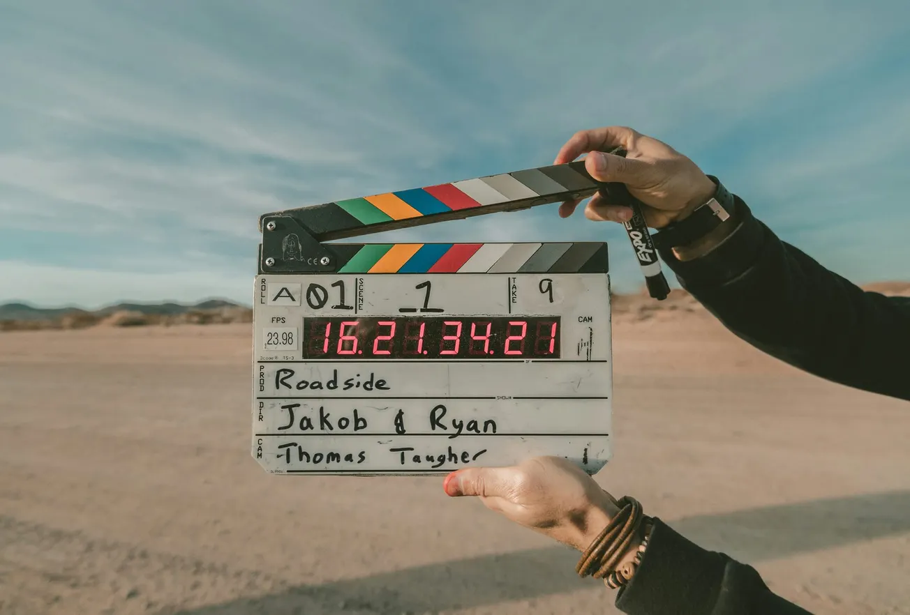 Person holding a film clapperboard in a desert setting under a clear sky, showing vibrant colored stripes and details of a scene take.