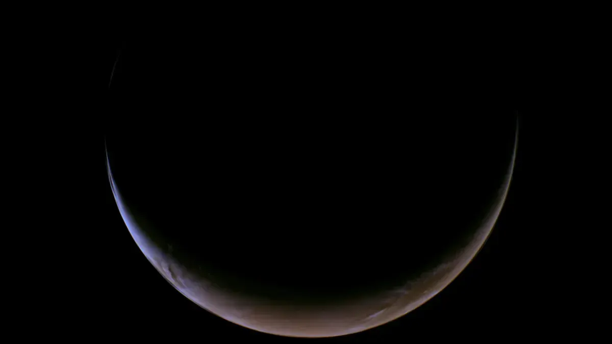 A crescent view of a planet's surface against a dark sky. The thin illuminated edge contrasts with the shadowed area, creating a serene and mysterious tone.