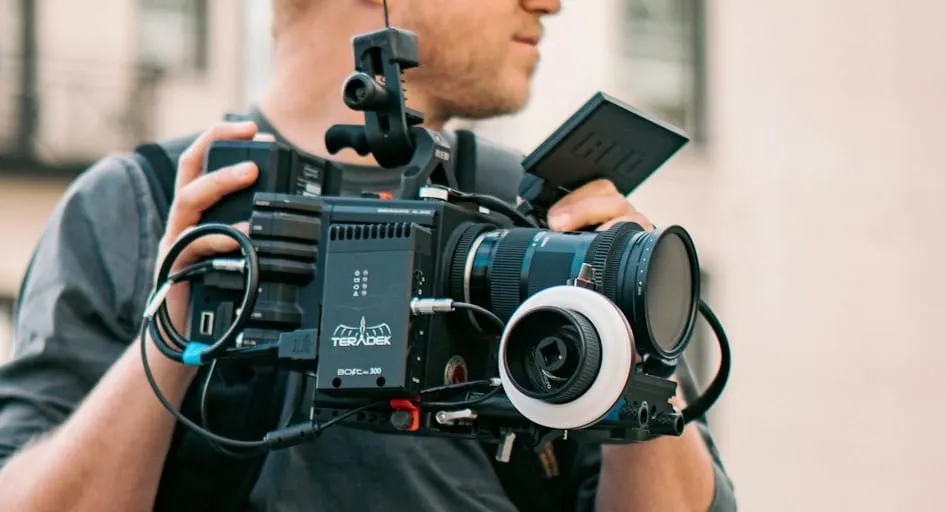 A videographer wearing an ergonomic camera support vest and rig, comfortably holding a large professional video camera and telephoto lens, emphasizing stability and reduced strain.