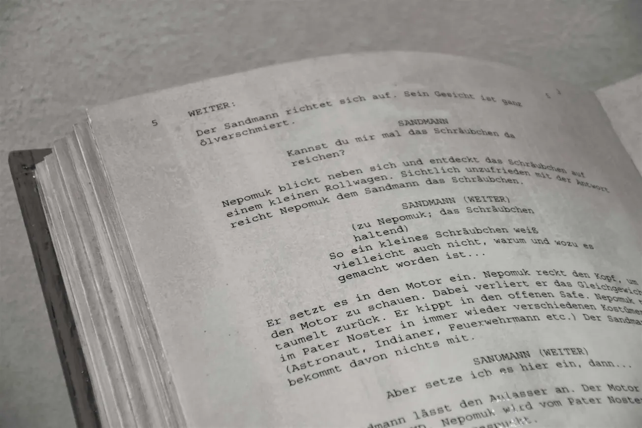 Close-up of an aged script page with typewritten German text and stage directions, conveying a vintage theatrical or cinematic feel.