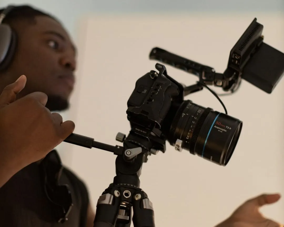 A focused content creator meticulously adjusts a compact mirrorless camera and microphone on a desk for optimal video podcast recording.