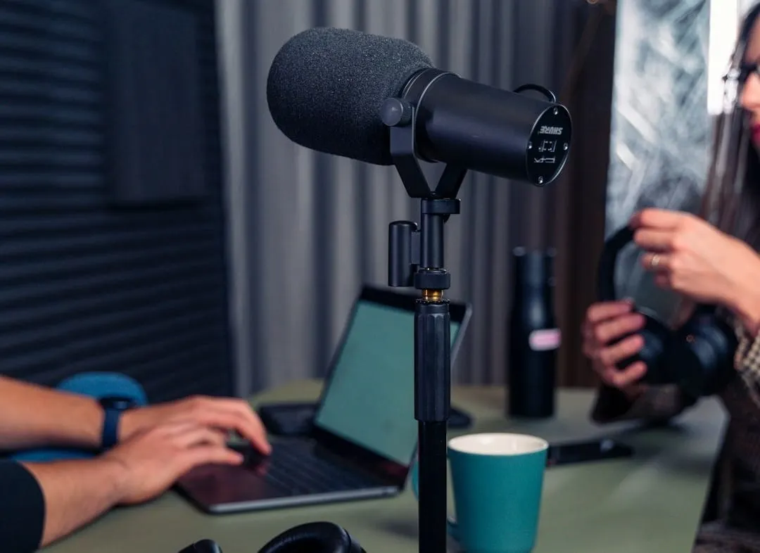 A diverse team of podcast creators collaborate in a well-equipped studio, looking at a laptop with data visualizations, symbolizing industry growth.