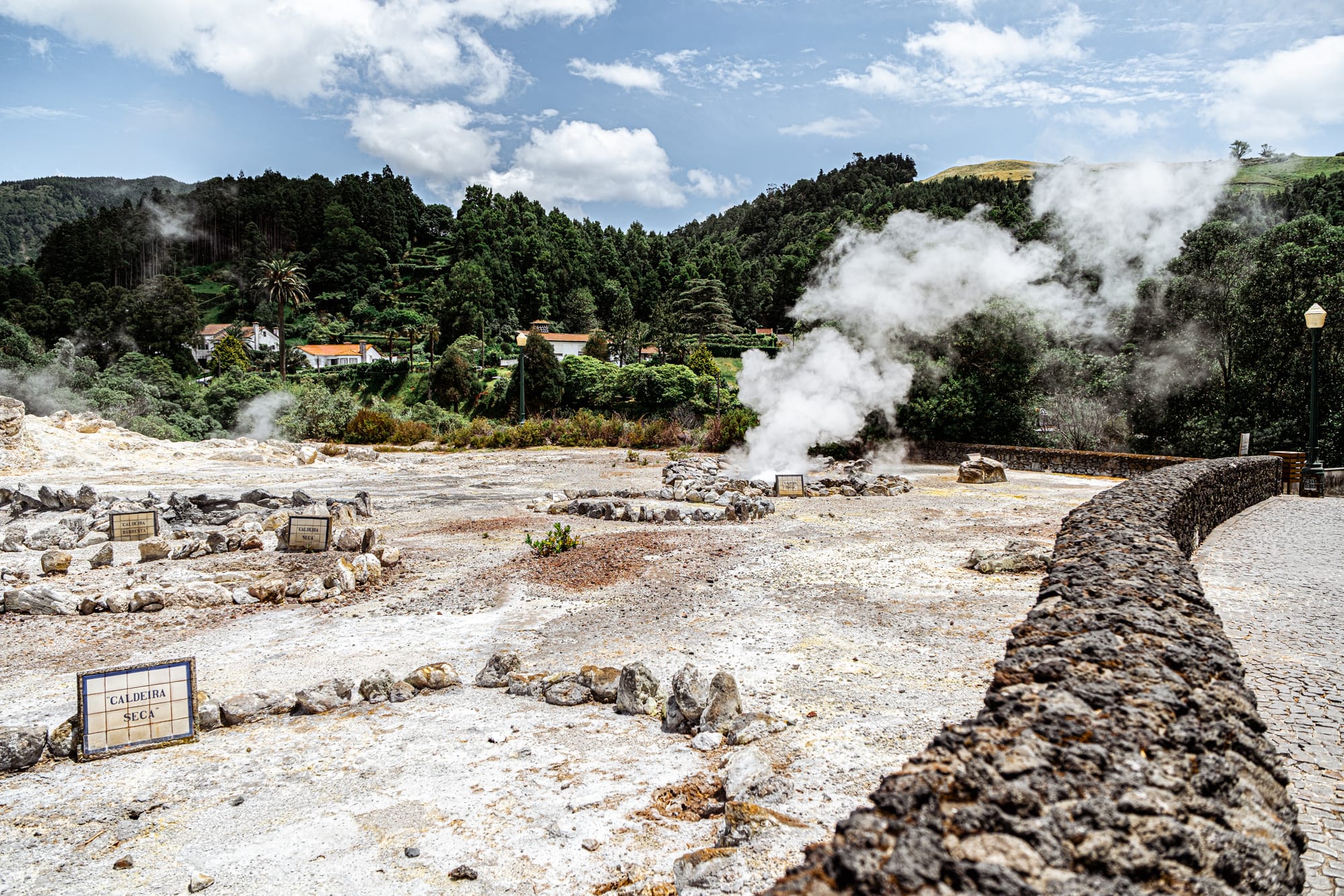 Geothermal steam rising from multiple caldeiras in a rocky thermal field surrounded by forest in Furnas