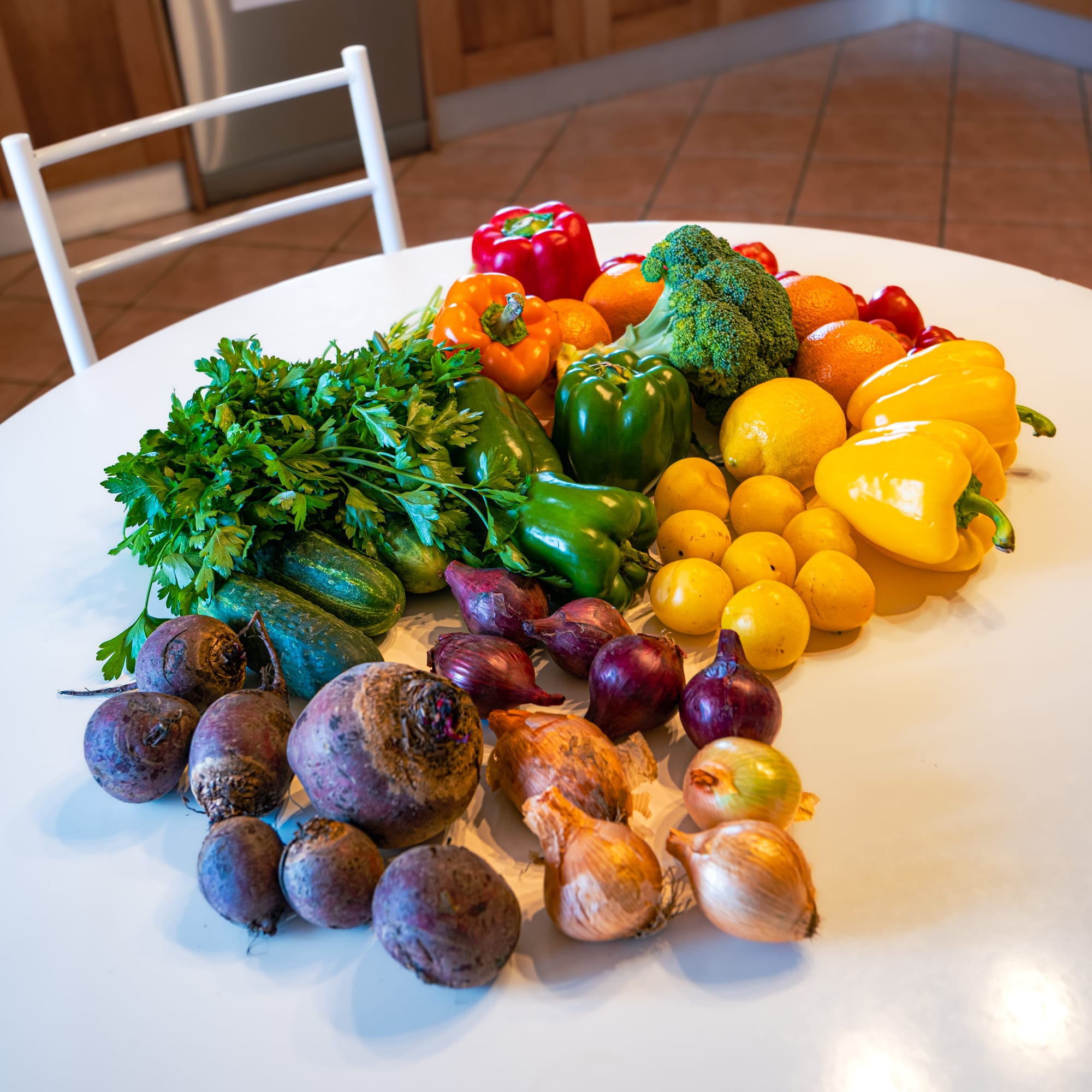 A colourful assortment of fresh produce from the farmers’ market laid out on a white table, including beets, onions, parsley, peppers, lemons, and broccoli