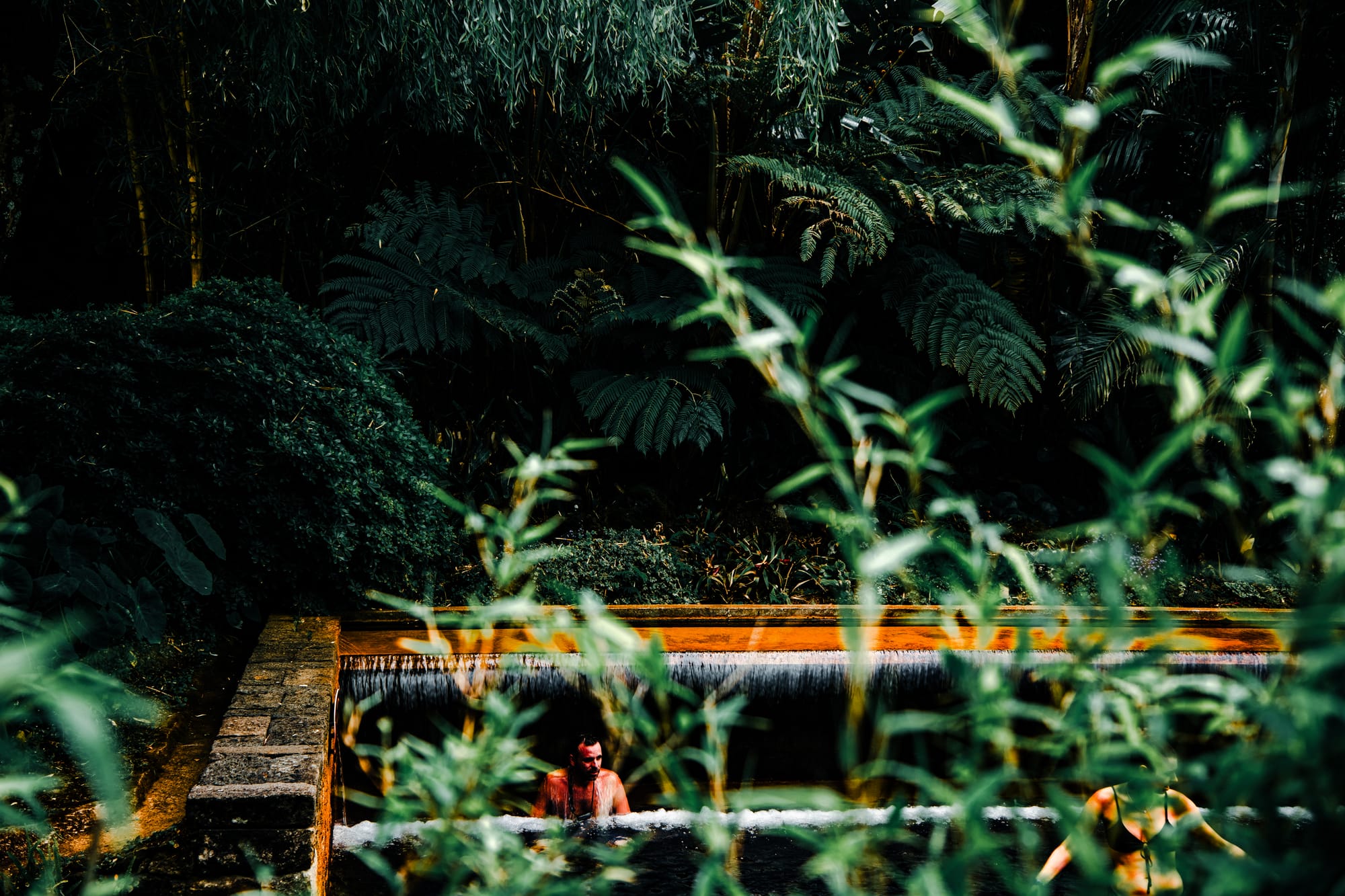 People bathing in a thermal pool surrounded by dense tropical foliage at Poça da Dona Beija