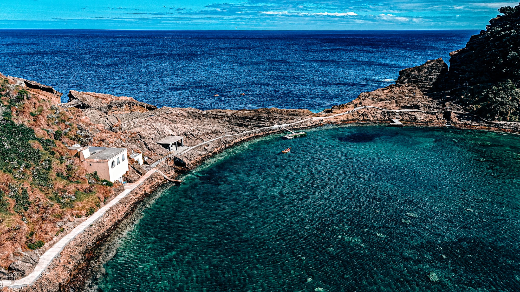 Aerial view of the circular lagoon within Ilhéu de Vila Franca do Campo, surrounded by volcanic rock, with a kayak floating in the calm, clear water