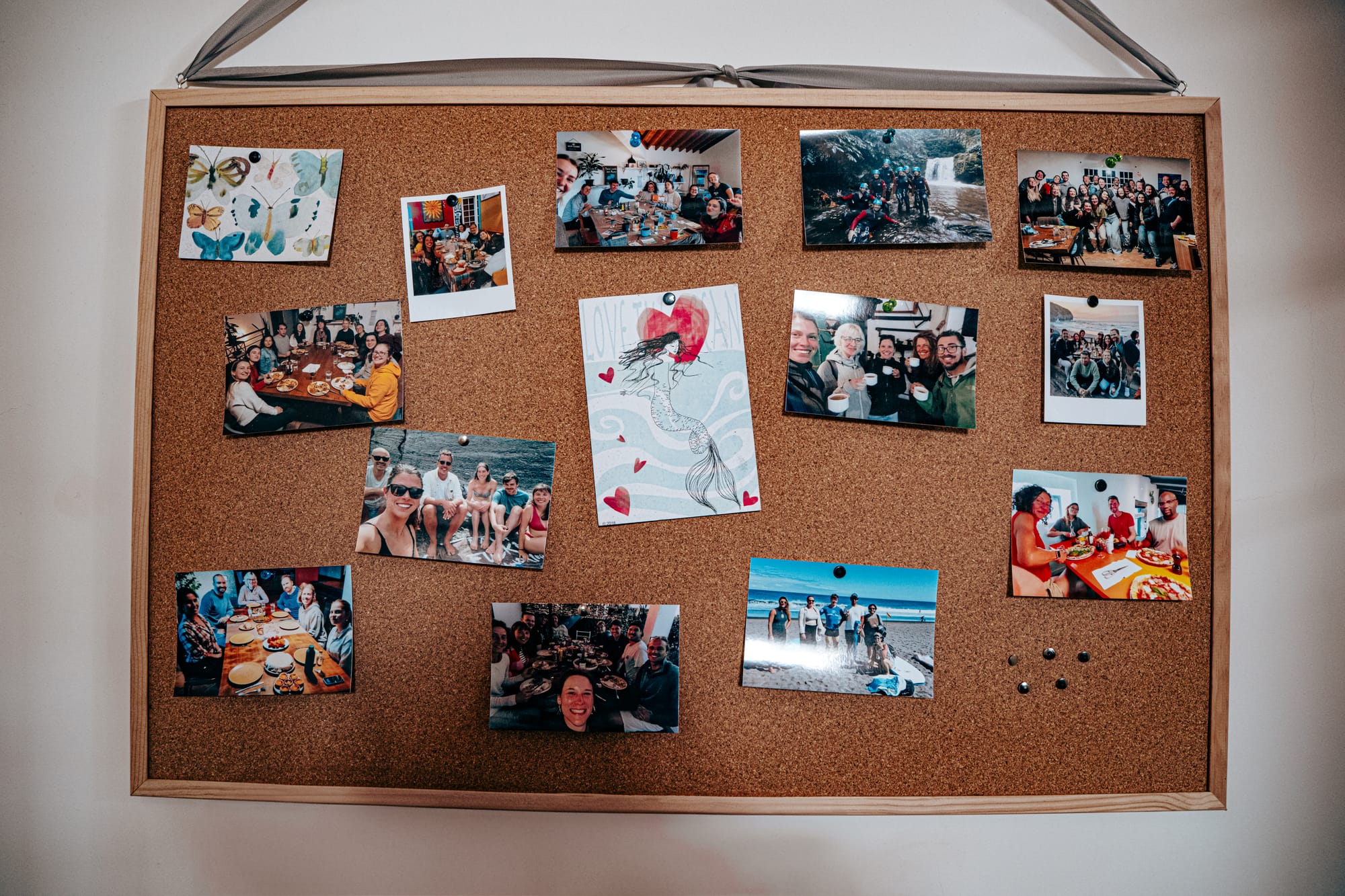 Corkboard filled with photographs of Lava Coliving guests during group meals, hikes, beach outings, and indoor activities