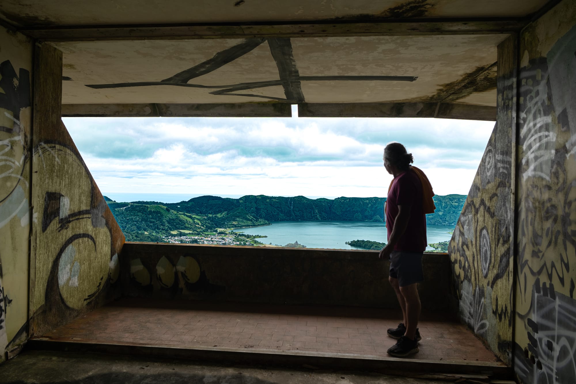 View of a man standing in a graffiti-covered room, overlooking the twin lakes of Sete Cidades on São Miguel Island, Azores
