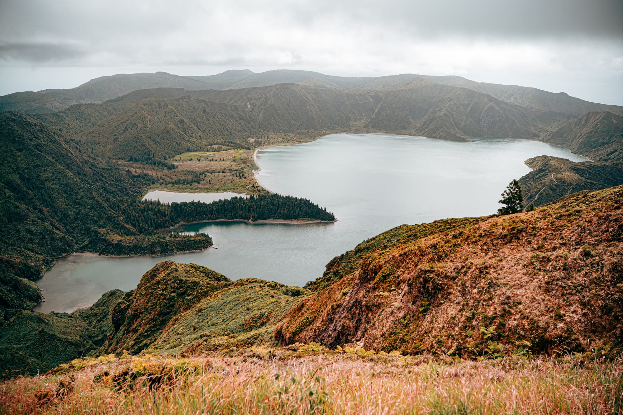 Expansive view of Lagoa do Fogo with forested hills, crater walls, and layered clouds above