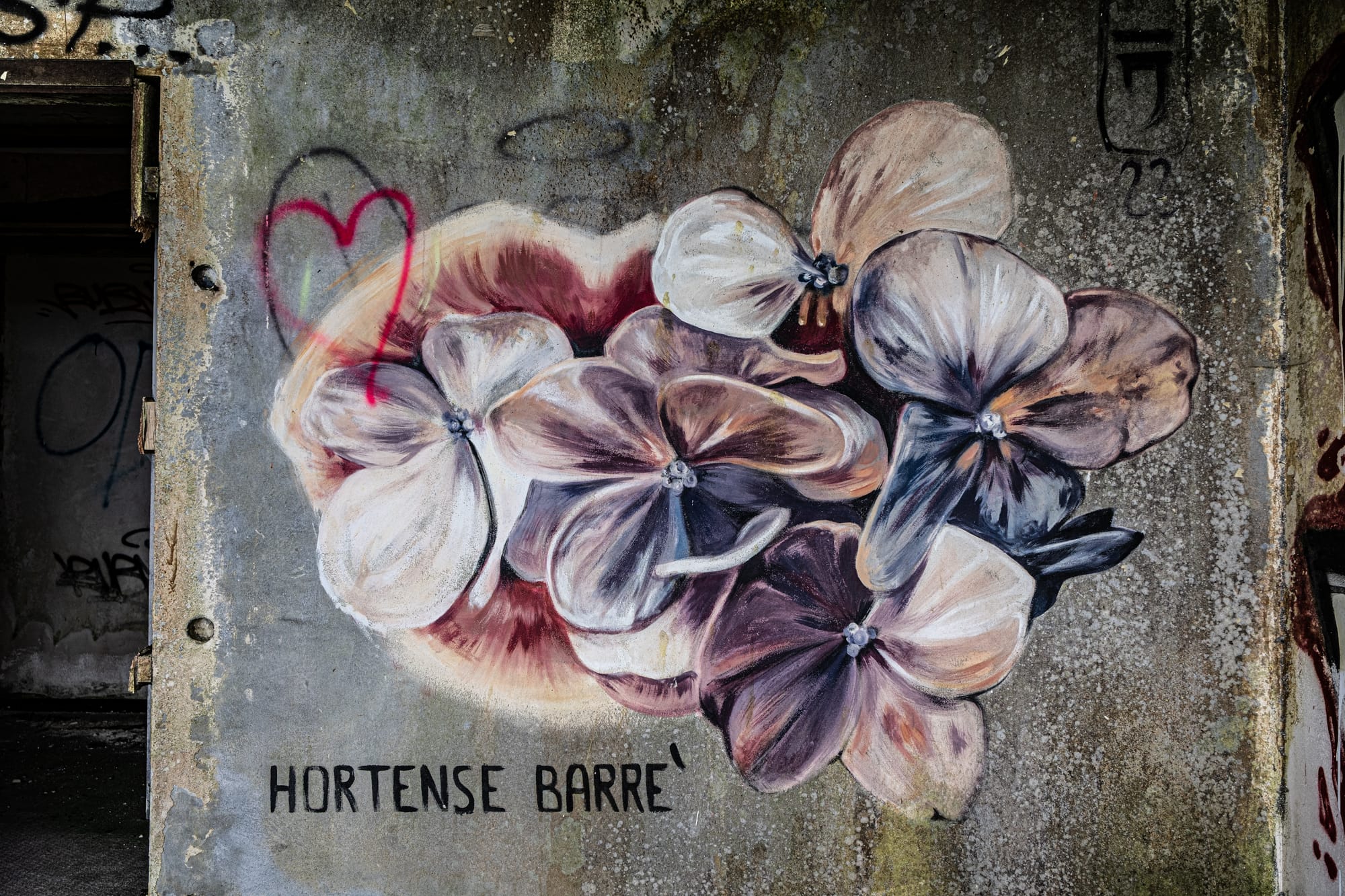 Wall mural of delicate, overlapping purple and cream-colored flowers with the artist’s signature “Hortense Barre” on a worn concrete surface inside the Monte Palace Hotel