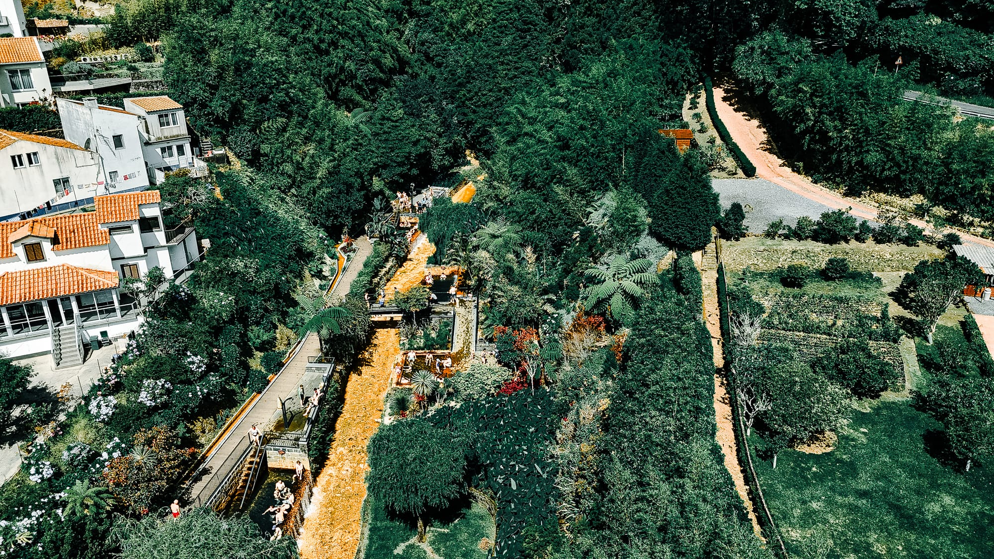 Aerial shot of Poça da Dona Beija hot springs surrounded by dense greenery and village rooftops