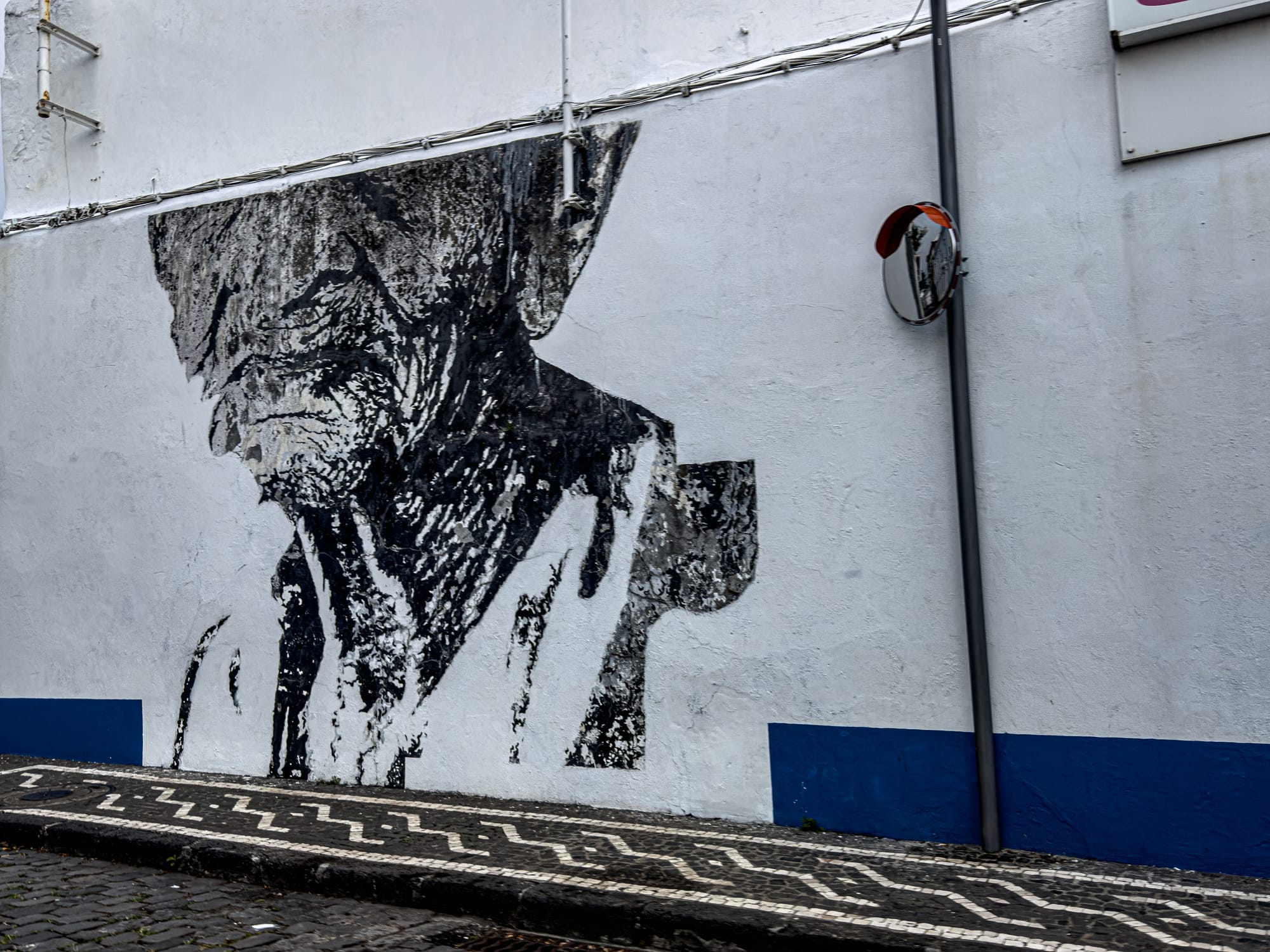 Black-and-white mural of an elderly man in traditional Azorean attire painted on a white wall in Ponta Delgada, partially weathered by time