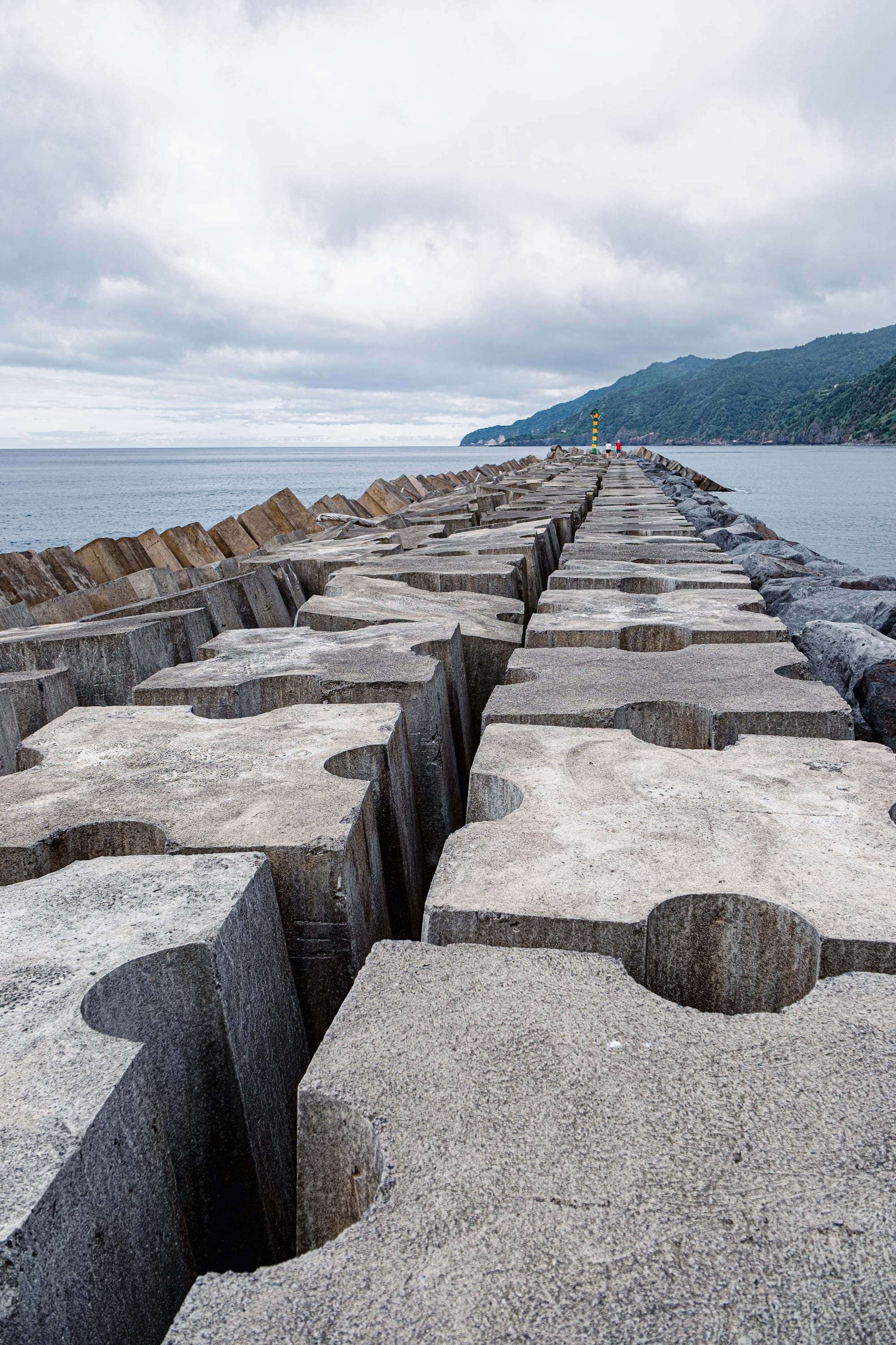Close-up view of large interlocking concrete blocks on the jetty in Povoação, São Miguel, stretching toward the sea with the coastline visible in the distance