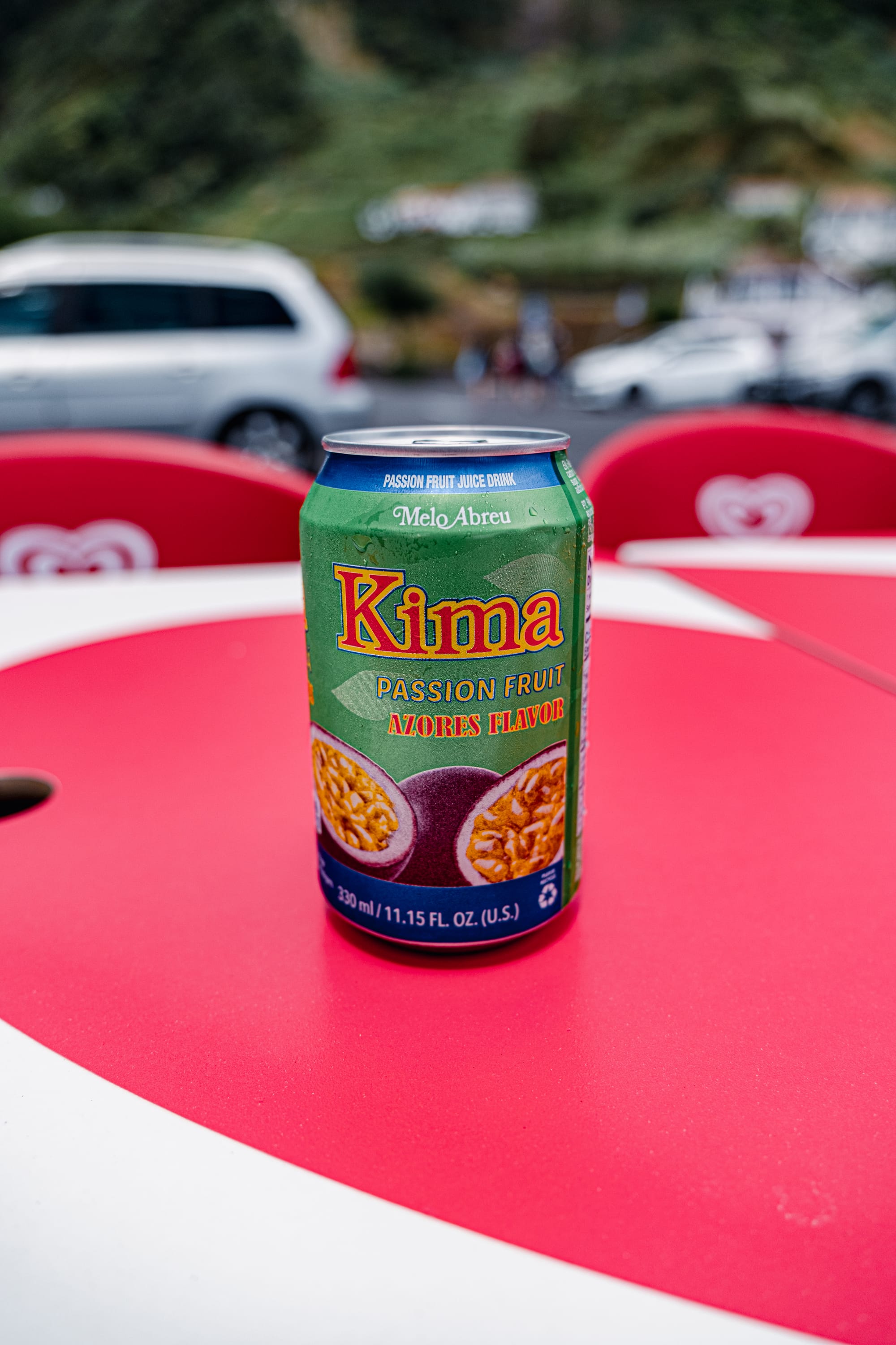 A close-up of a cold can of Kima passionfruit soda on a bright red table in the Azores