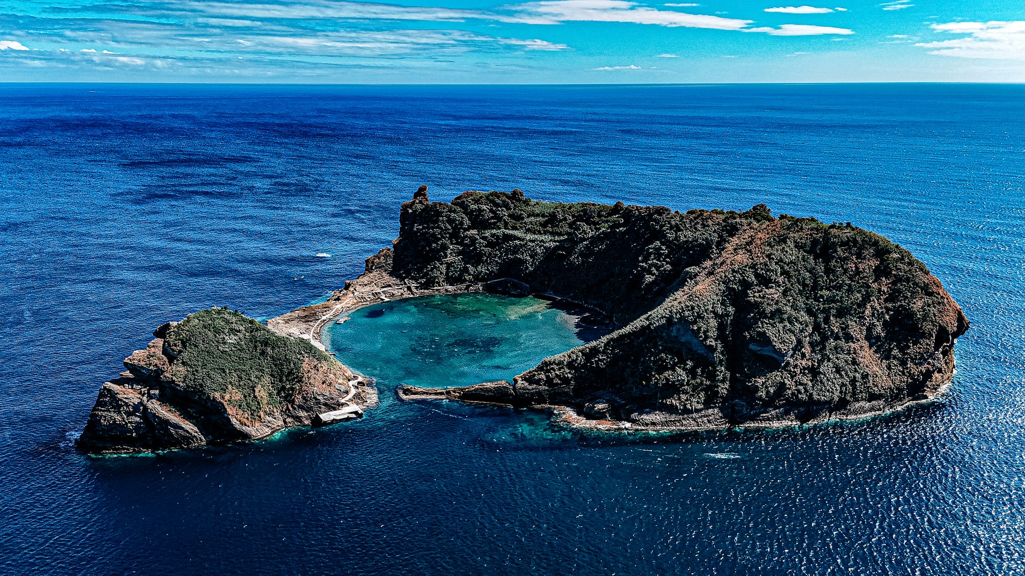 Aerial view of Ilhéu de Vila Franca do Campo, a volcanic islet off the coast of São Miguel, with a circular lagoon surrounded by rugged cliffs and deep blue Atlantic waters—popular for kayaking, snorkeling, and nature watching