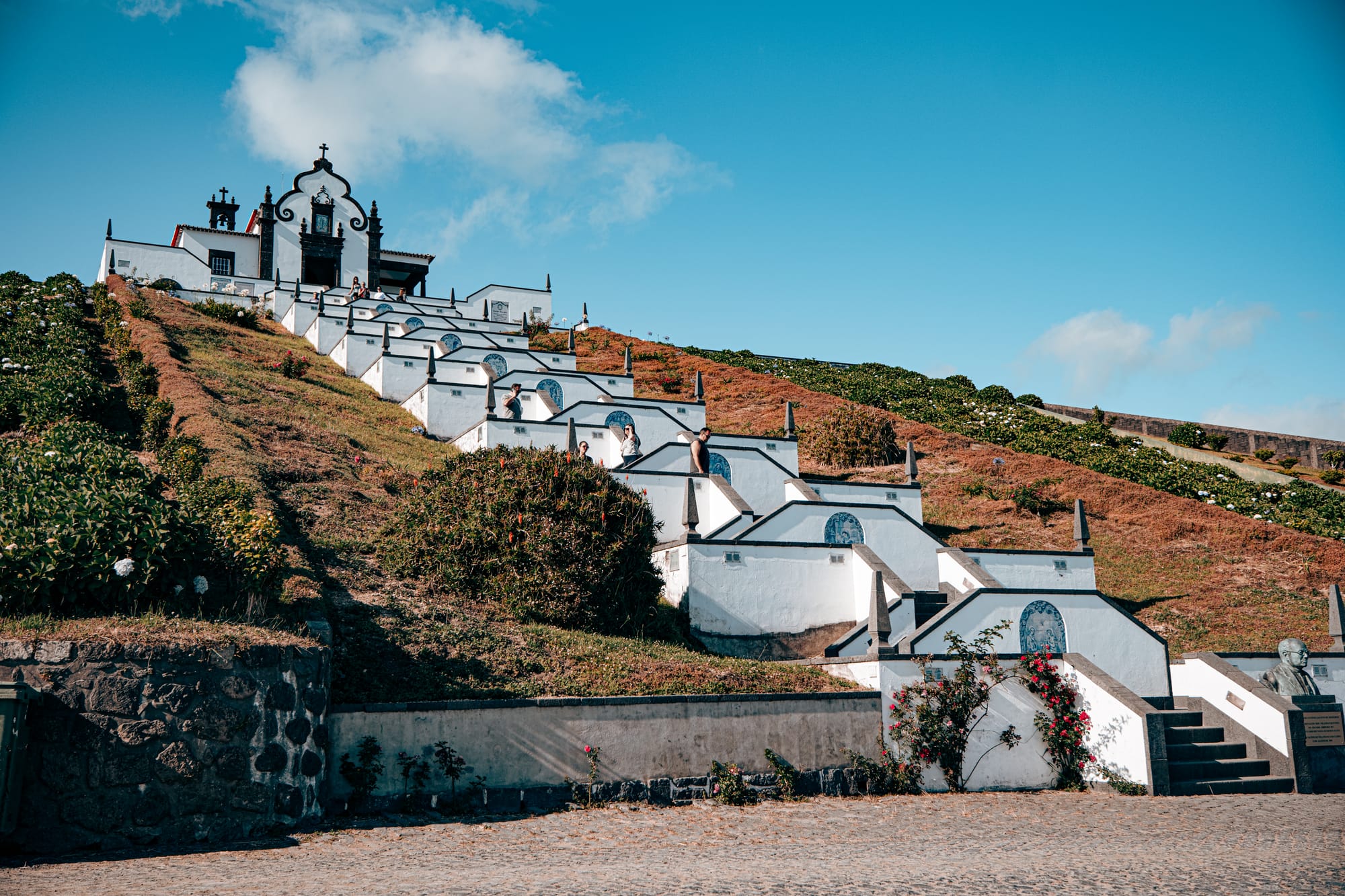 White chapel atop a terraced hillside with symmetrical staircases and azulejo tiles leading up through flowering gardens to the Santuário de Nossa Senhora da Paz
