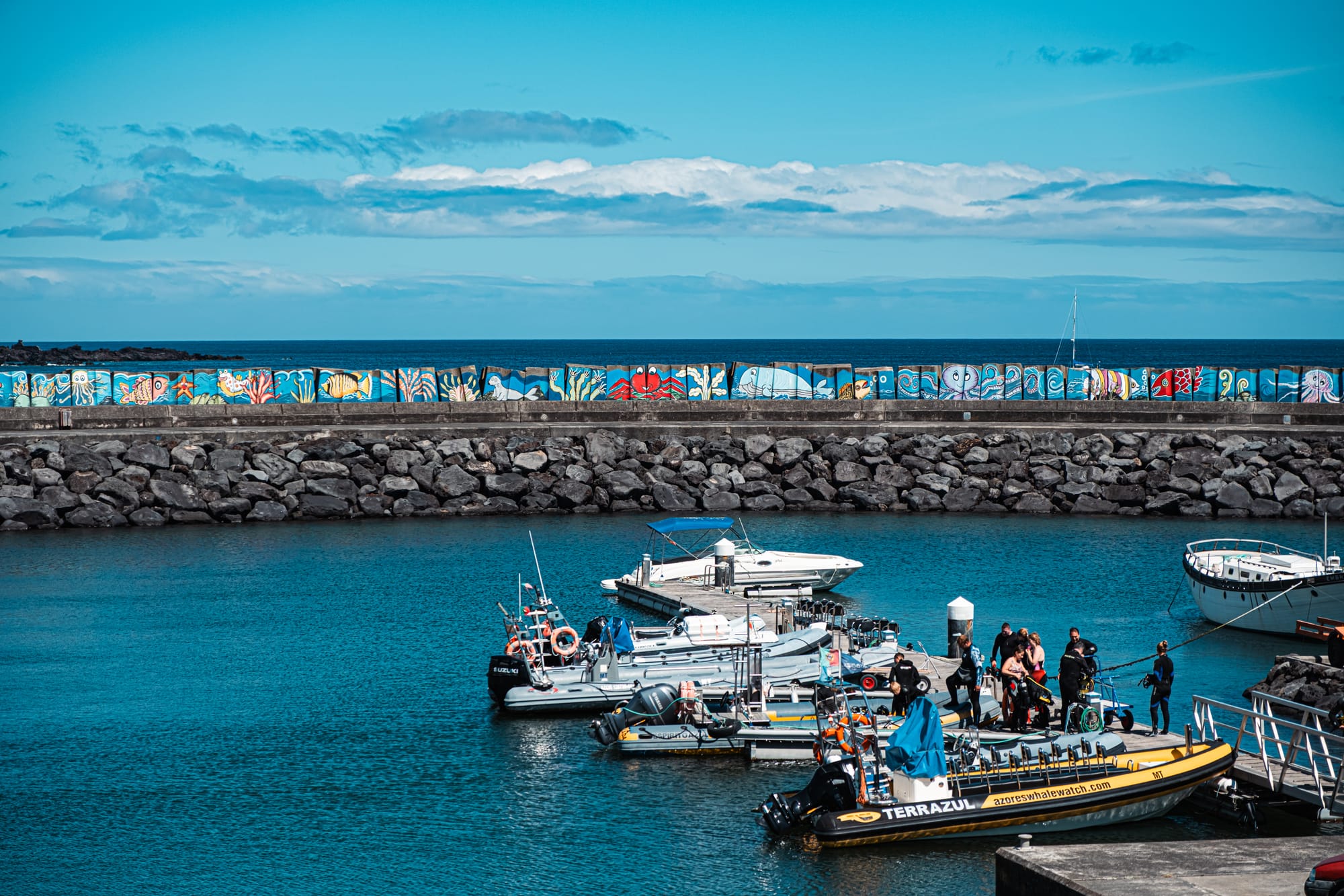 Colorful mural-lined breakwater and tour boats in the marina at Vila Franca do Campo