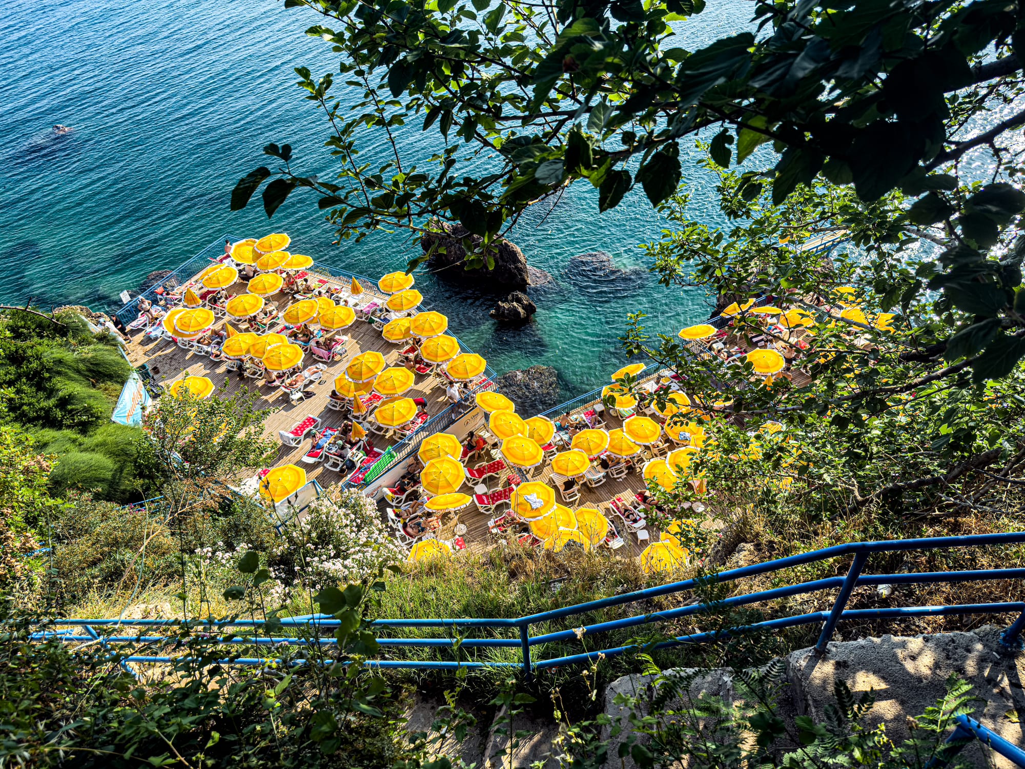View through greenery of yellow umbrellas and cliffside sun decks at İnciraltı Beach in Antalya, Turkey