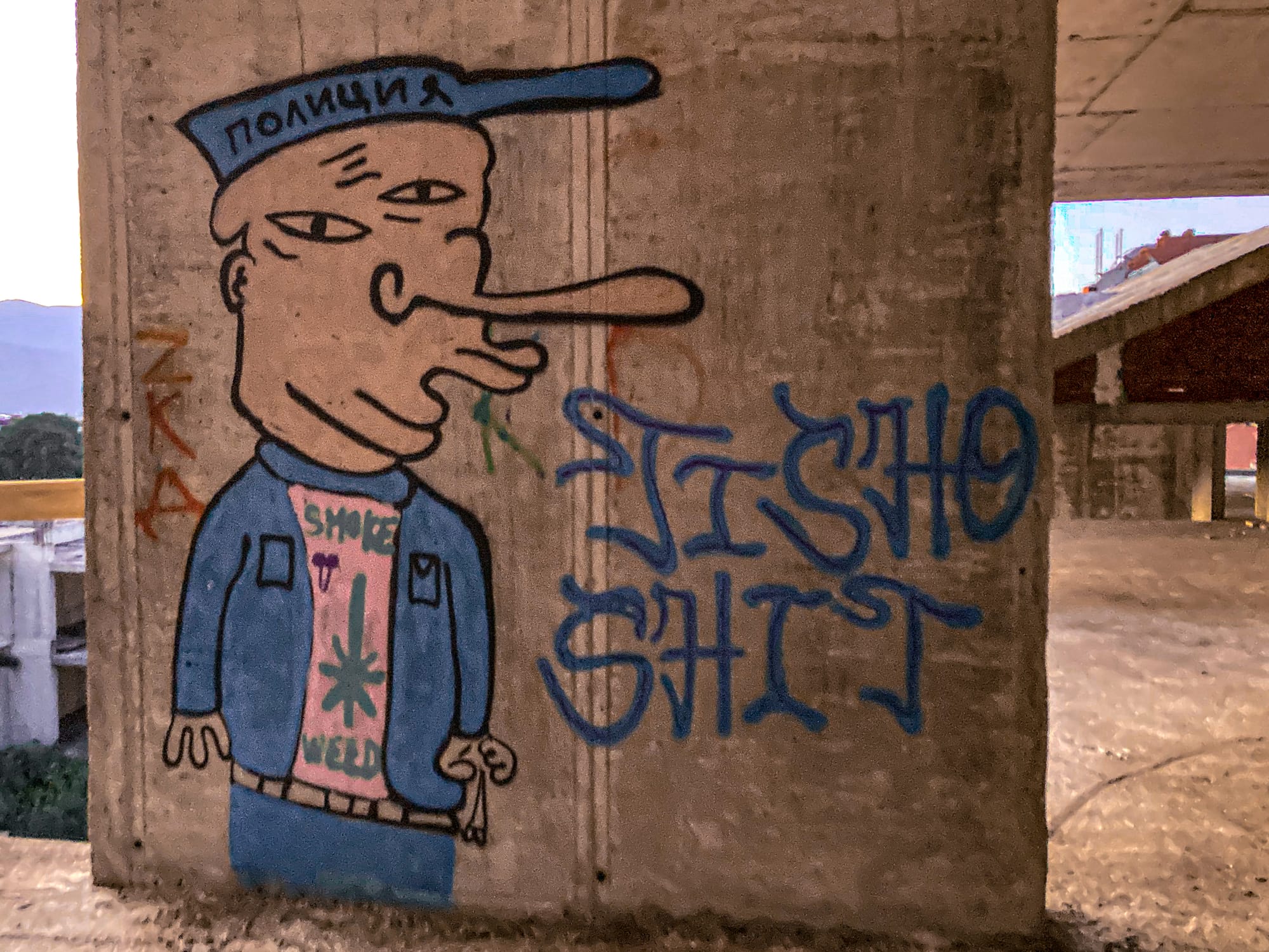 Cartoon-style graffiti of a distorted figure wearing a blue jacket and cap with Cyrillic text, painted on the wall of an unfinished building in Bansko, Bulgaria