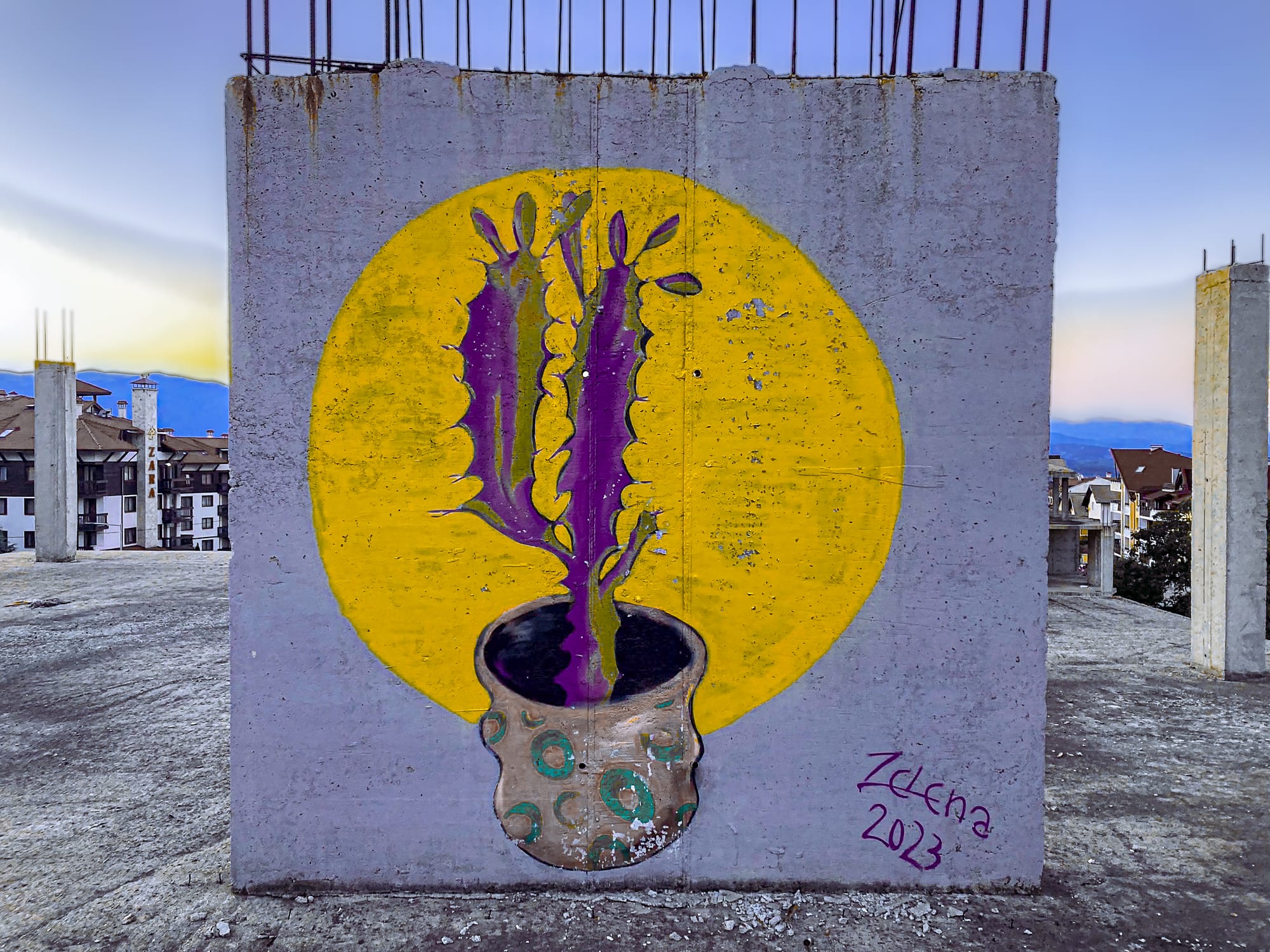 Street art mural of a potted plant with purple stems and green leaves against a bright yellow circle, painted on the concrete wall of an abandoned building in Bansko, Bulgaria