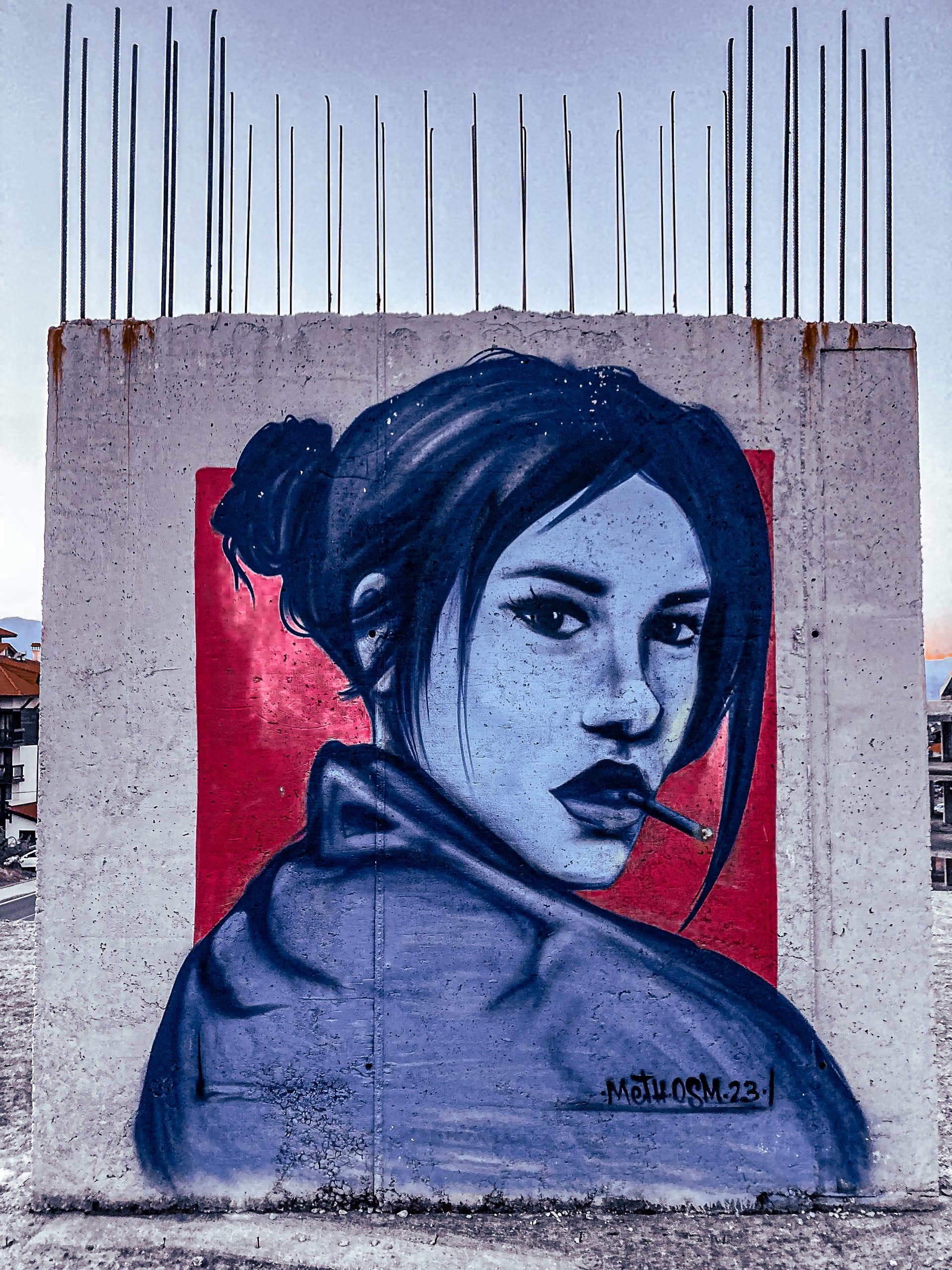 Street art mural of a woman with dark hair and a cigarette, painted in blue and red on the concrete wall of an abandoned building in Bansko, Bulgaria