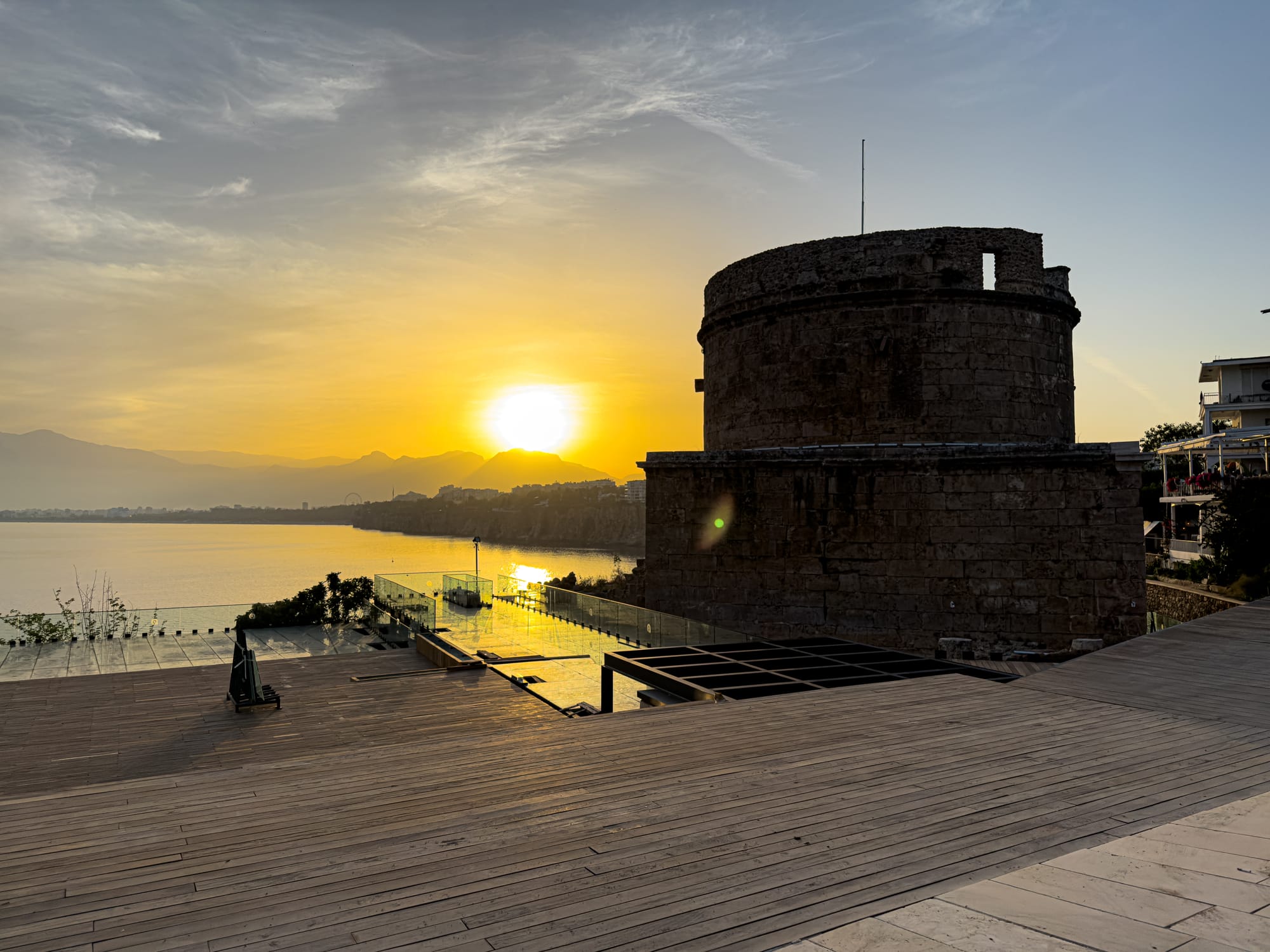 Hıdırlık Tower in Antalya silhouetted against a vibrant sunset over the sea and mountains
