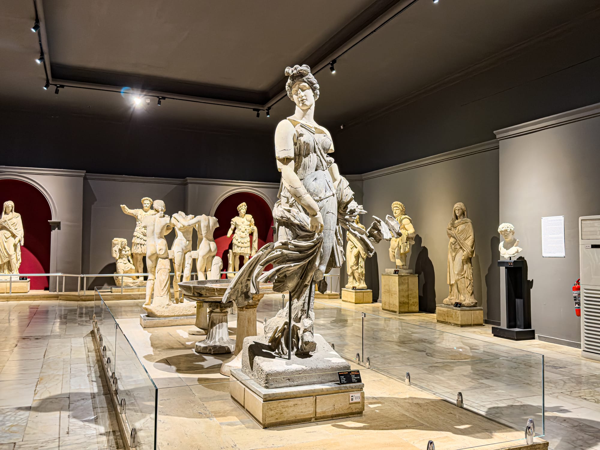 Interior of Antalya’s Archaeological Museum showing a large central statue of a woman in motion, surrounded by other Greco-Roman sculptures in a spacious, well-lit hall