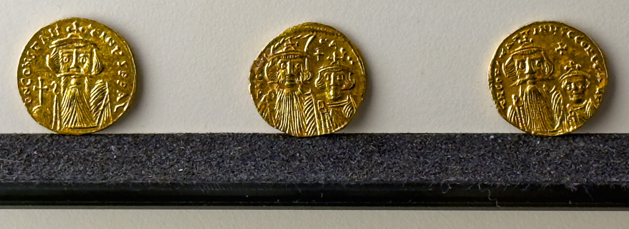 Three ancient gold coins with Byzantine-style engravings, displayed in a row on a dark felt surface