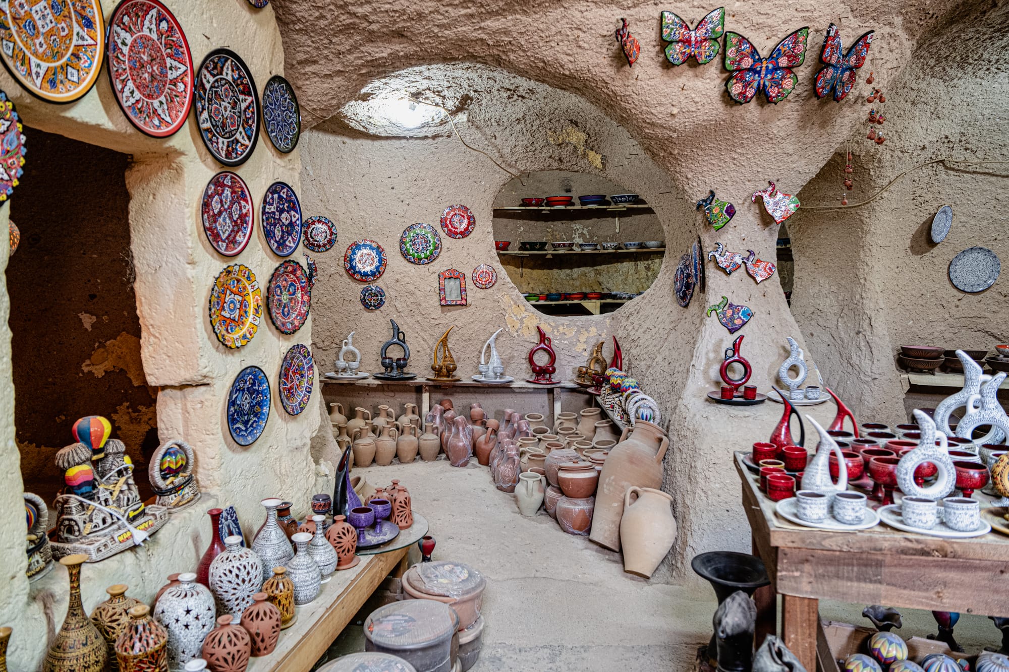 Interior of a pottery shop in Avanos, Cappadocia, displaying colorful ceramic plates, vases, and decorative pieces arranged on shelves and tables within a cave
