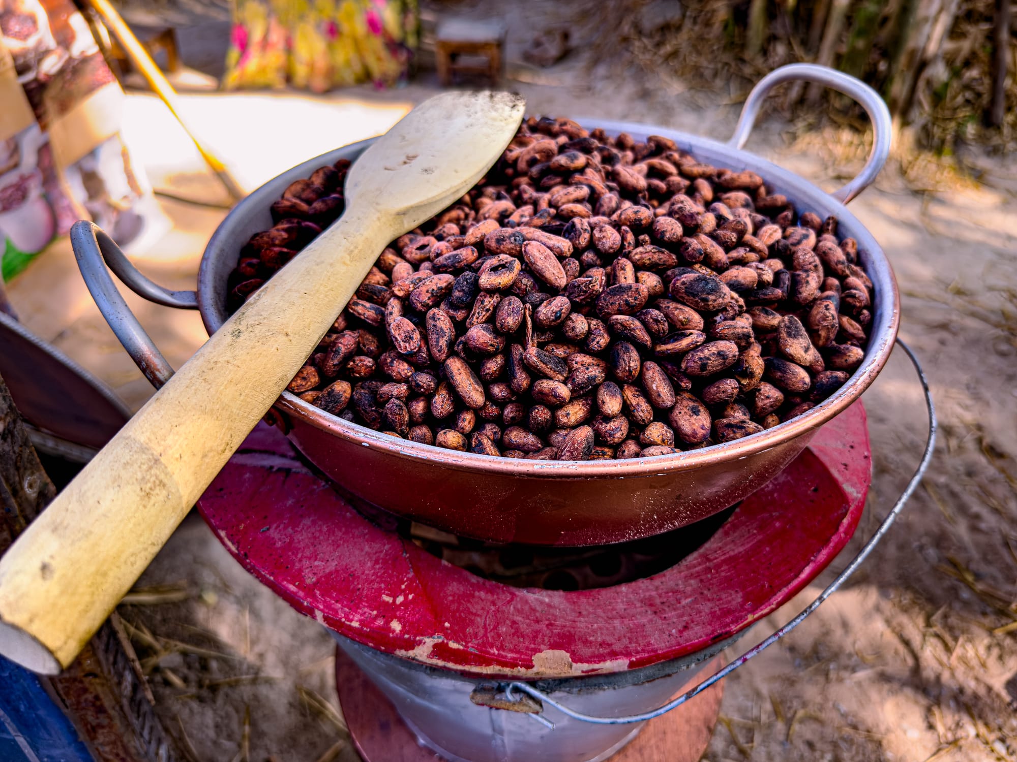 A close-up of a metal pan filled with freshly roasted cacao beans and a wooden spoon, displayed at the Bamboo Saturday Market in Chiang Mai