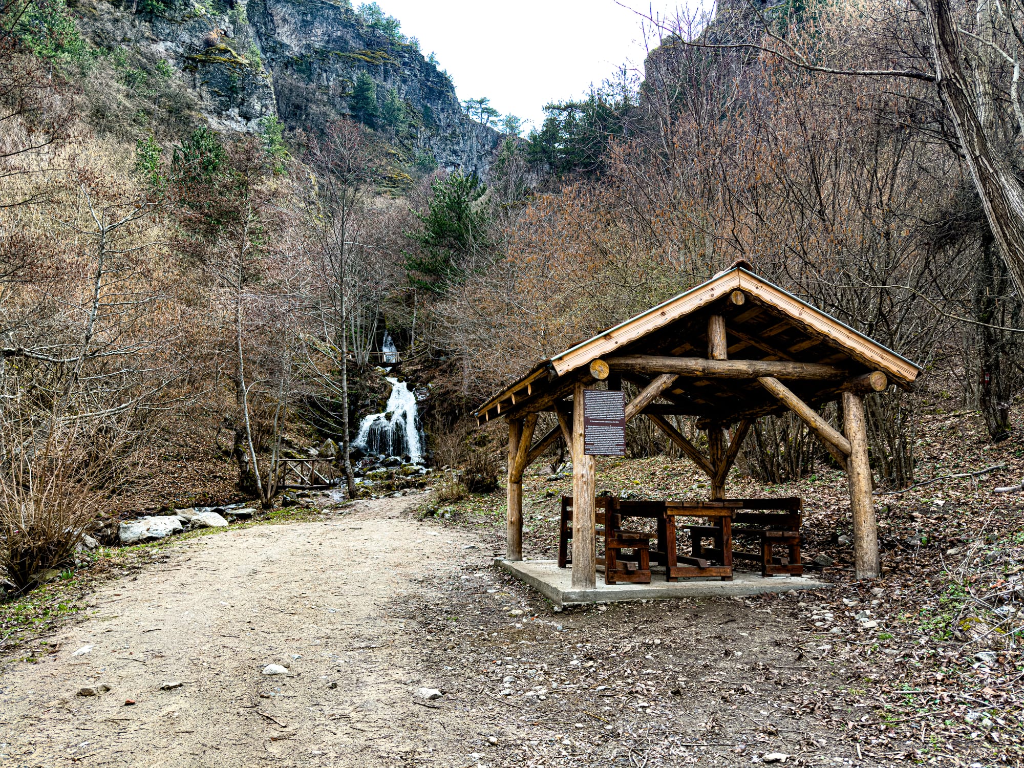 St. Nicholas Waterfall near Bansko, Bulgaria, cascading down a rocky slope with a wooden picnic shelter and benches set along the trail