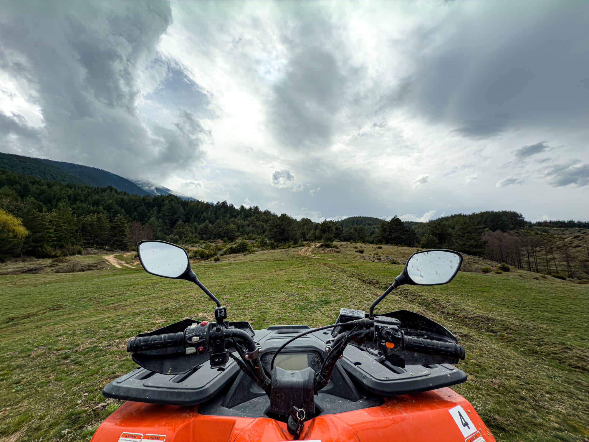 View from the seat of an ATV looking out across grassy meadows and forested hills near Bansko, Bulgaria, under a cloudy sky