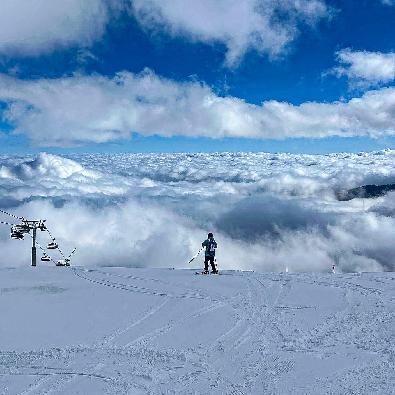 A skier stands on a snowy slope in Bansko’s Pirin Mountains, overlooking a breathtaking sea of clouds with a ski lift to the left
