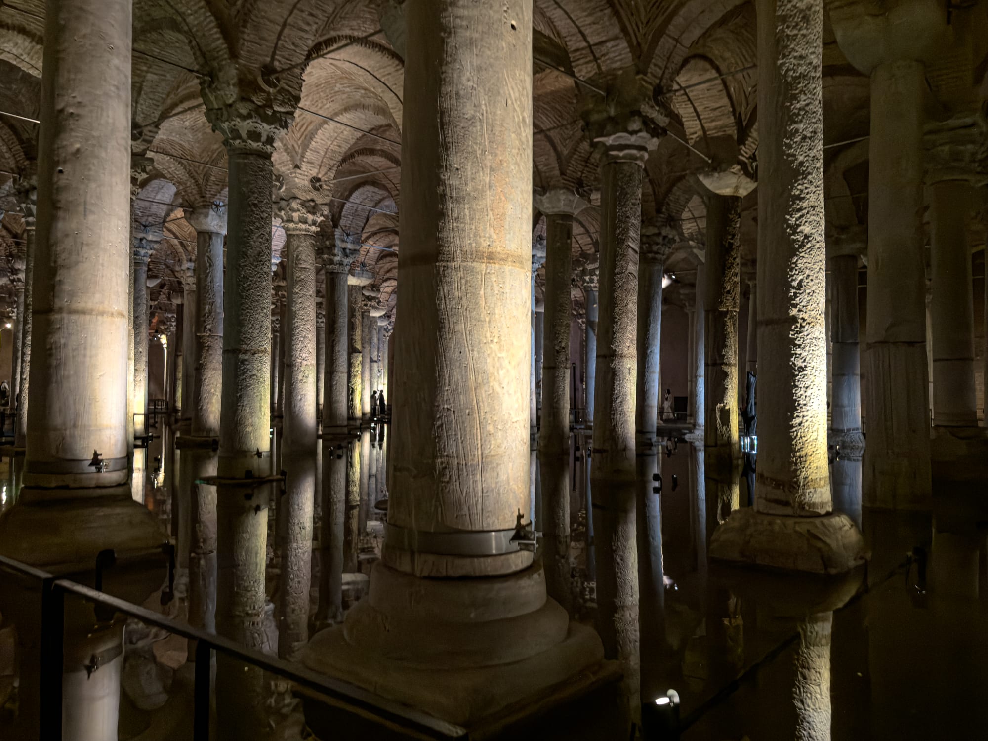 Interior view of the Basilica Cistern with rows of illuminated stone columns reflected in shallow water, creating a dramatic and moody atmosphere beneath arched ceilings