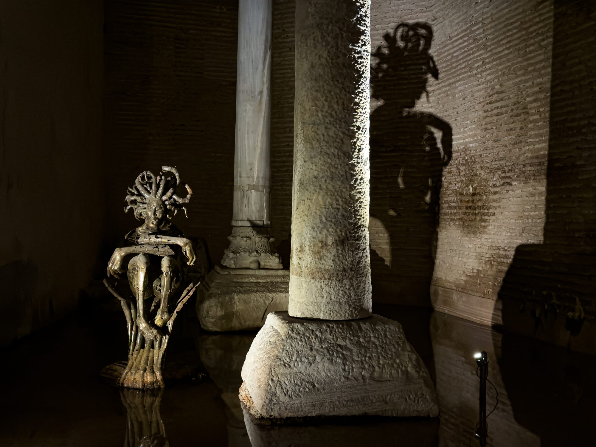Bronze Medusa-like sculpture with a dramatic shadow behind it in the Basilica Cistern, Istanbul