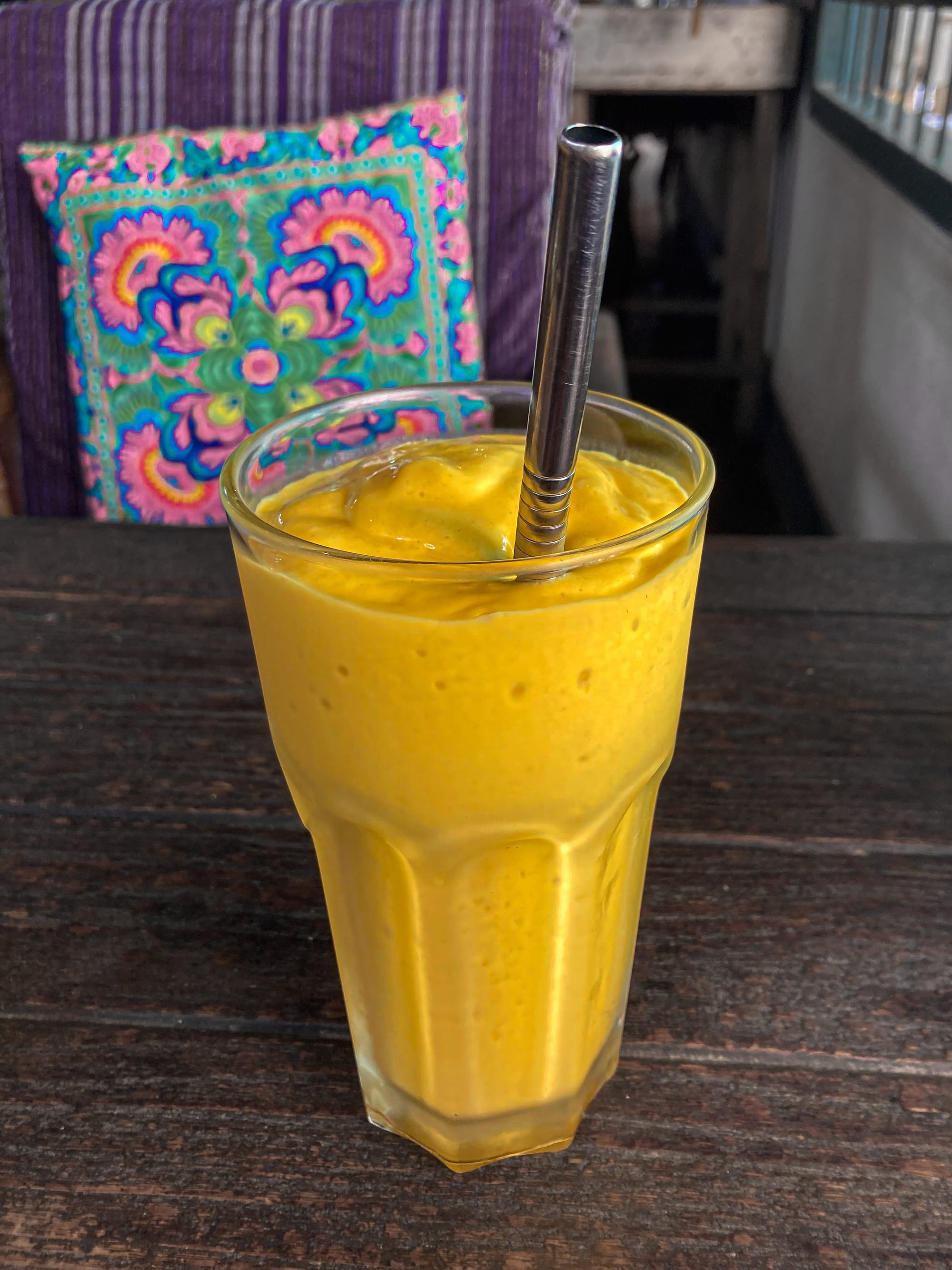Glass of Bird’s Nest Café’s mango coconut smoothie, thick and creamy with a bright golden color, served with a reusable metal straw on a wooden table