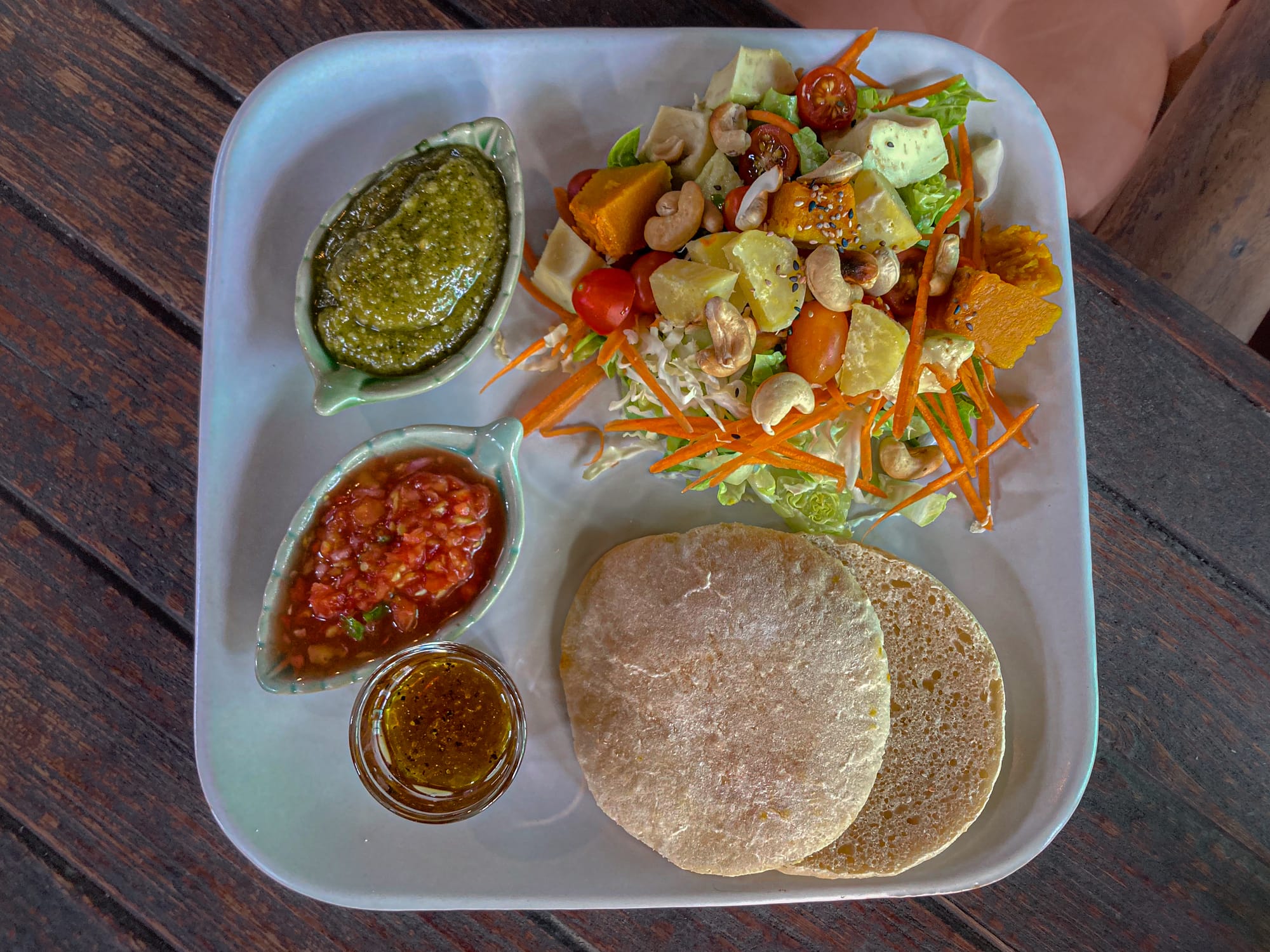 Colorful salad plate at Bird’s Nest Café in Chiang Mai with a mix of lettuce, carrots, cherry tomatoes, pumpkin, and cashews, served alongside two rounds of homemade pita bread, fresh green pesto, tomato salsa, and a small glass of dressing