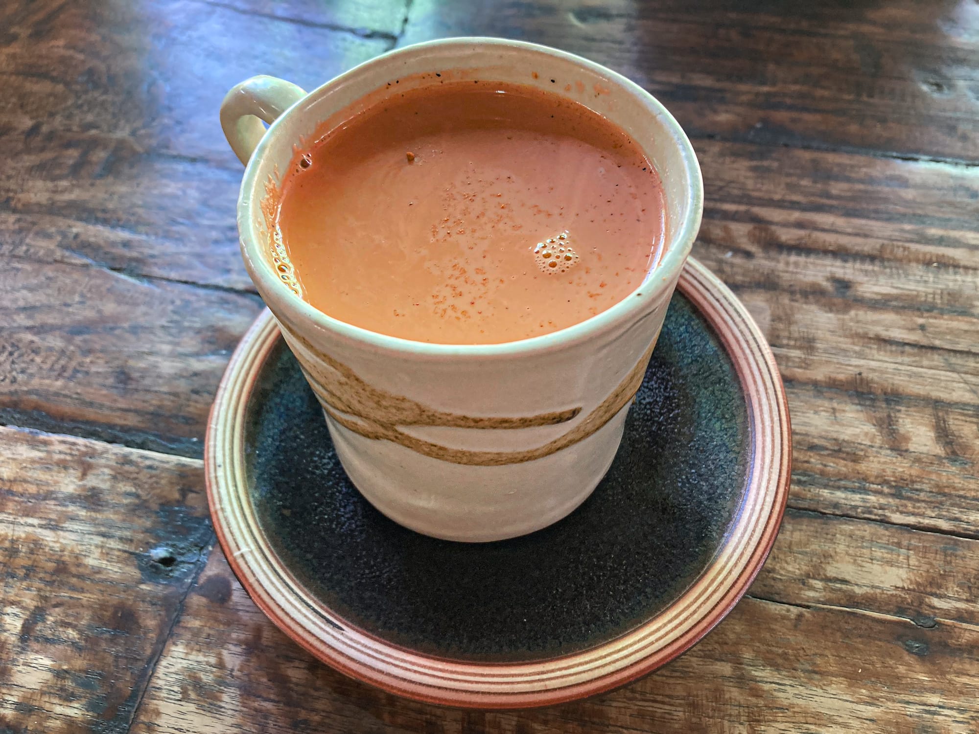 Cup of Thai tea at Bird’s Nest Café in Chiang Mai, rich orange in color, served in a handmade ceramic cup with matching saucer on a rustic wooden table