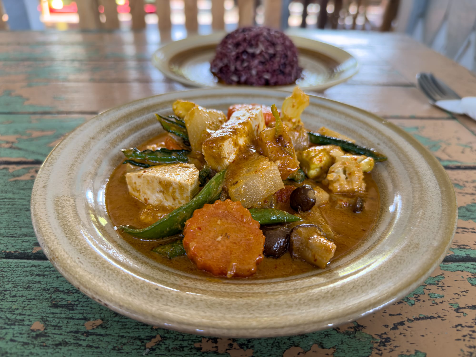 Panang curry at Bird’s Nest Café in Chiang Mai with tofu, carrots, green beans, and mushrooms in a rich coconut-based sauce, served with a side of purple rice