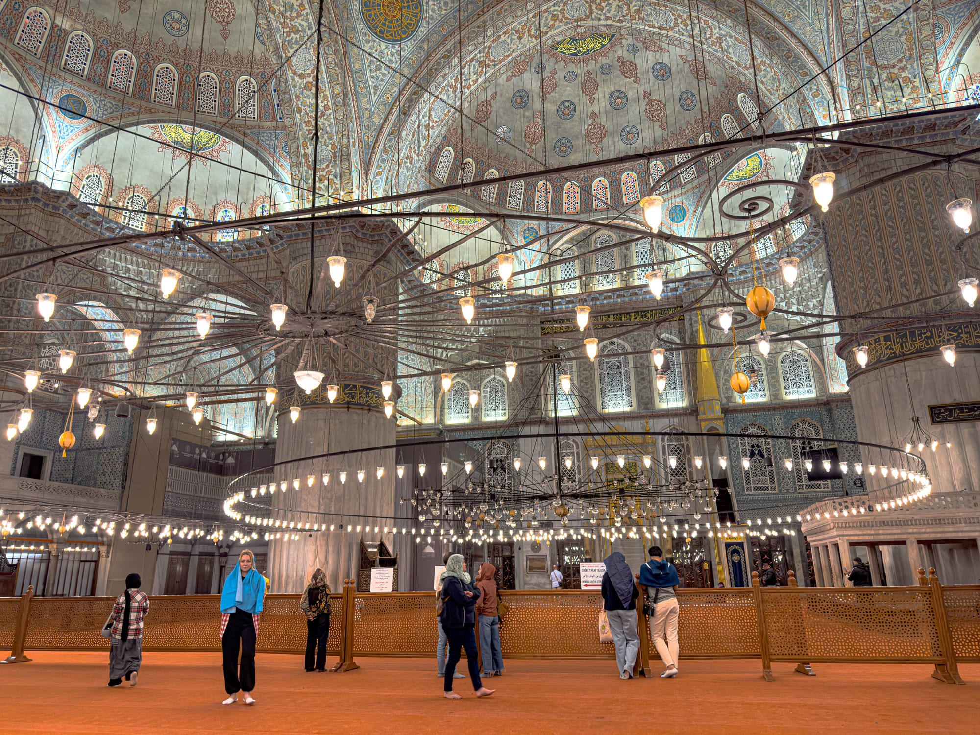 Visitors stand beneath the cascading chandeliers of the Blue Mosque, surrounded by intricate tilework and soaring domes