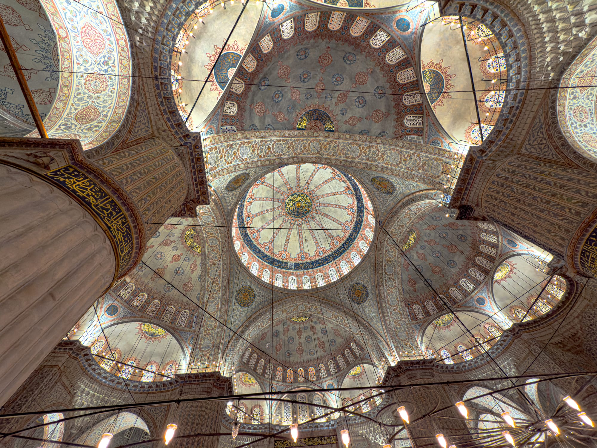 Looking up at the central dome of the Blue Mosque, showcasing intricate Iznik tilework and calligraphy