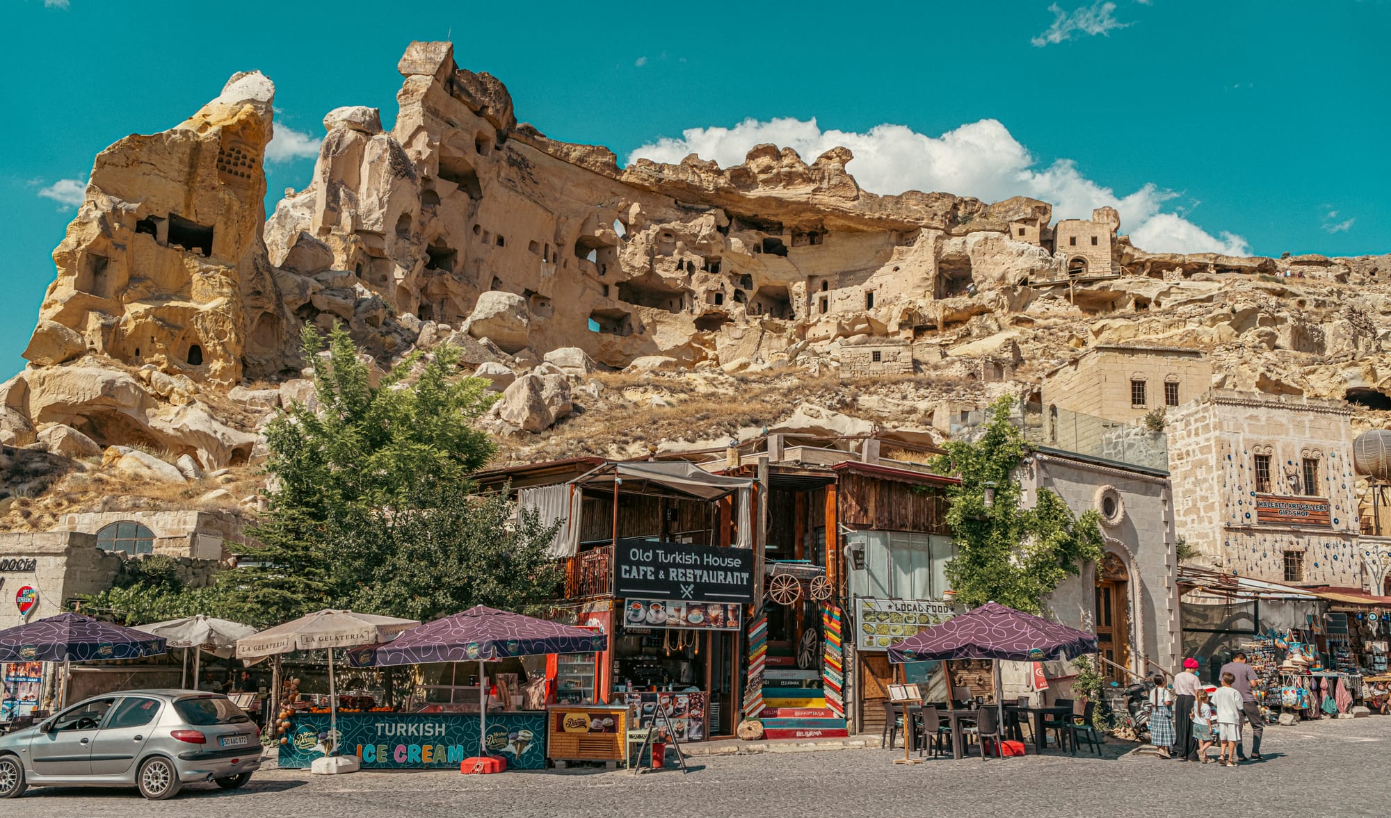 Street view of cafés, shops, and market stalls at the base of Çavuşin Castle in Cappadocia