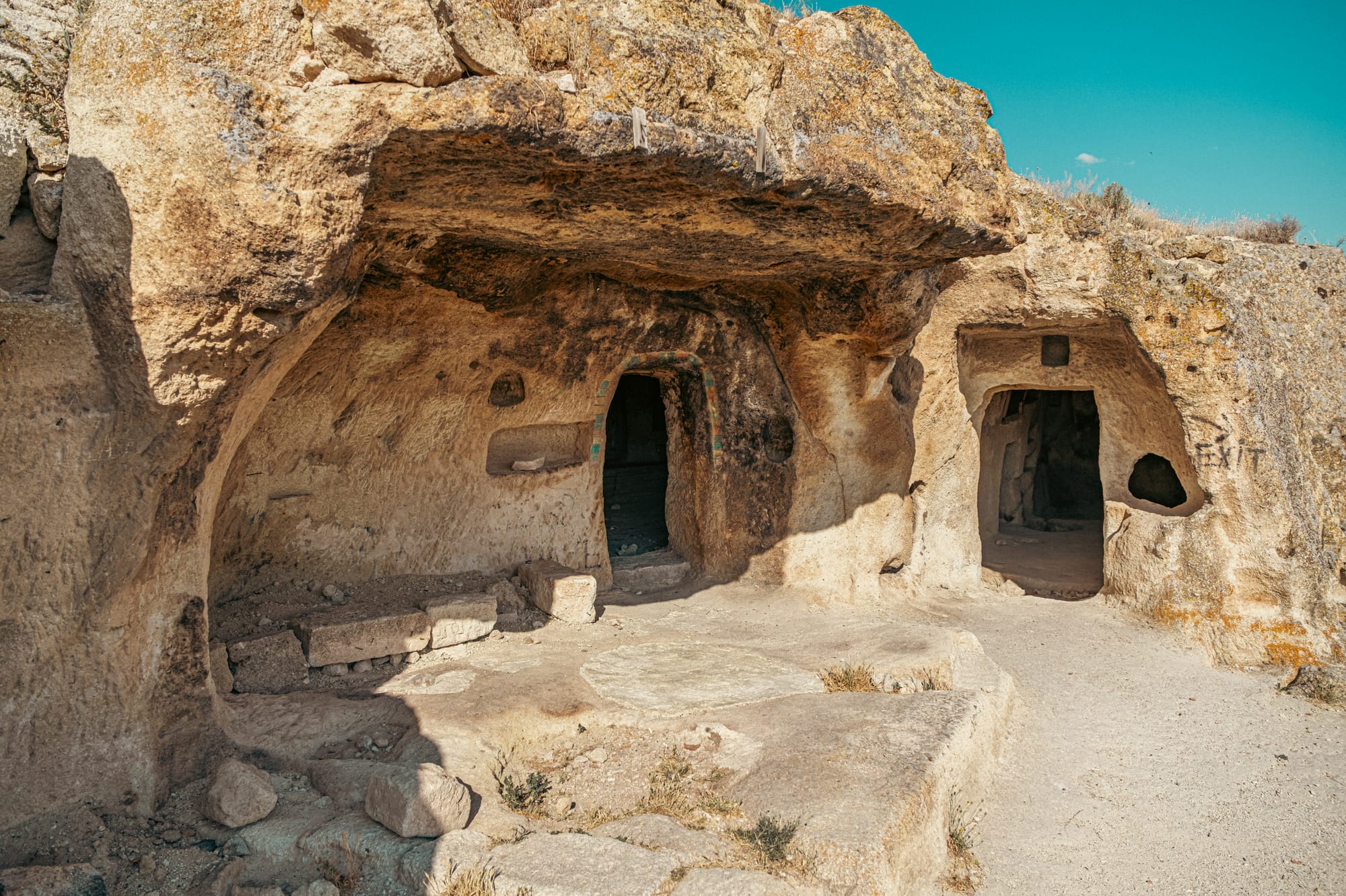 Ancient rock-cut cave entrance in Çavuşin Cappadocia with carved doorways and stone benches