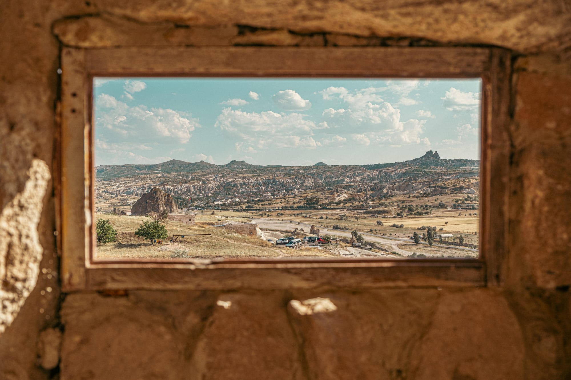 View of Cappadocia’s valleys and rock formations through a rectangular stone-framed window in Çavuşin Castle