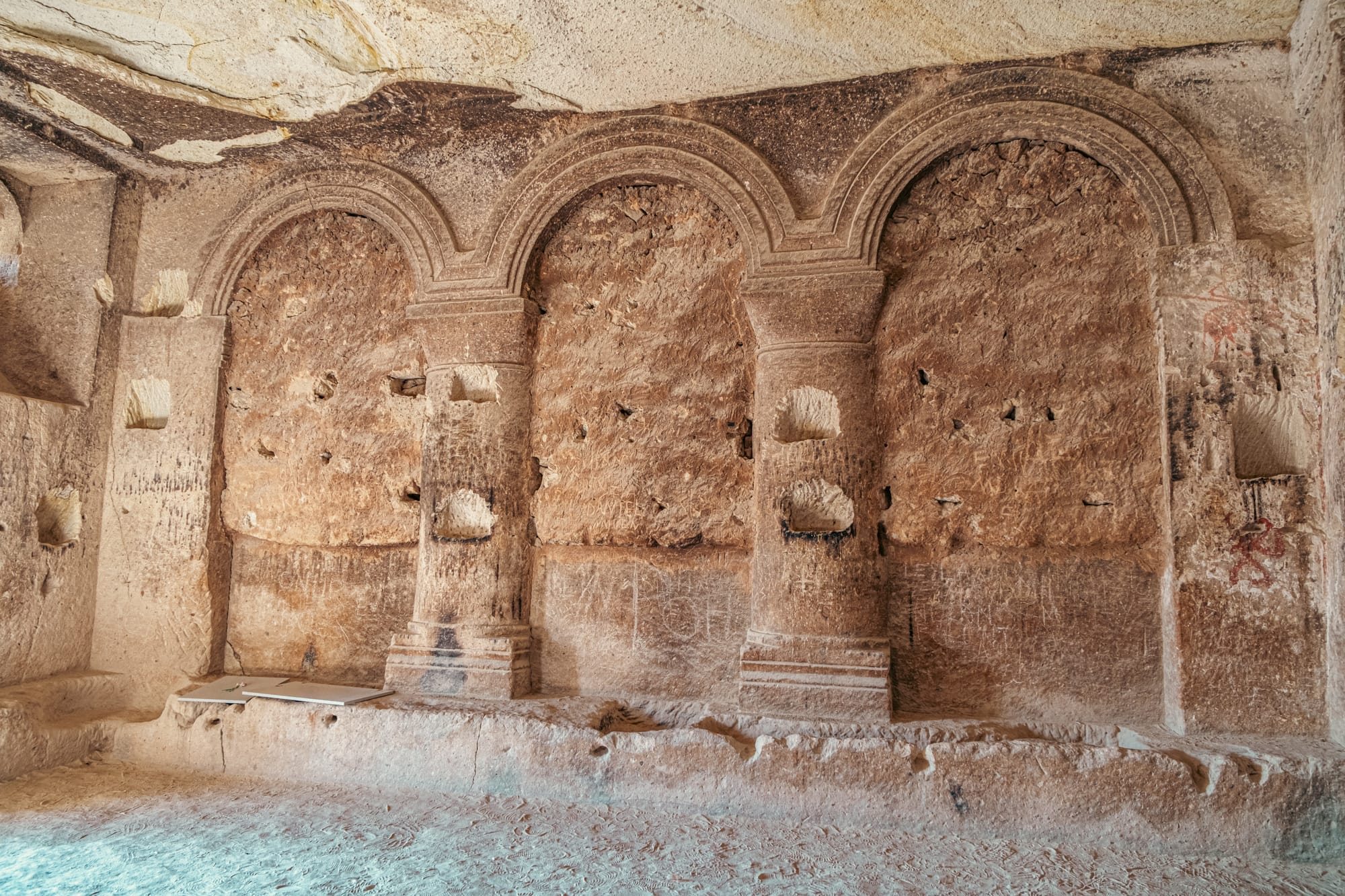 Intricately carved stone arches and columns inside a cave chamber at Çavuşin Castle in Cappadocia