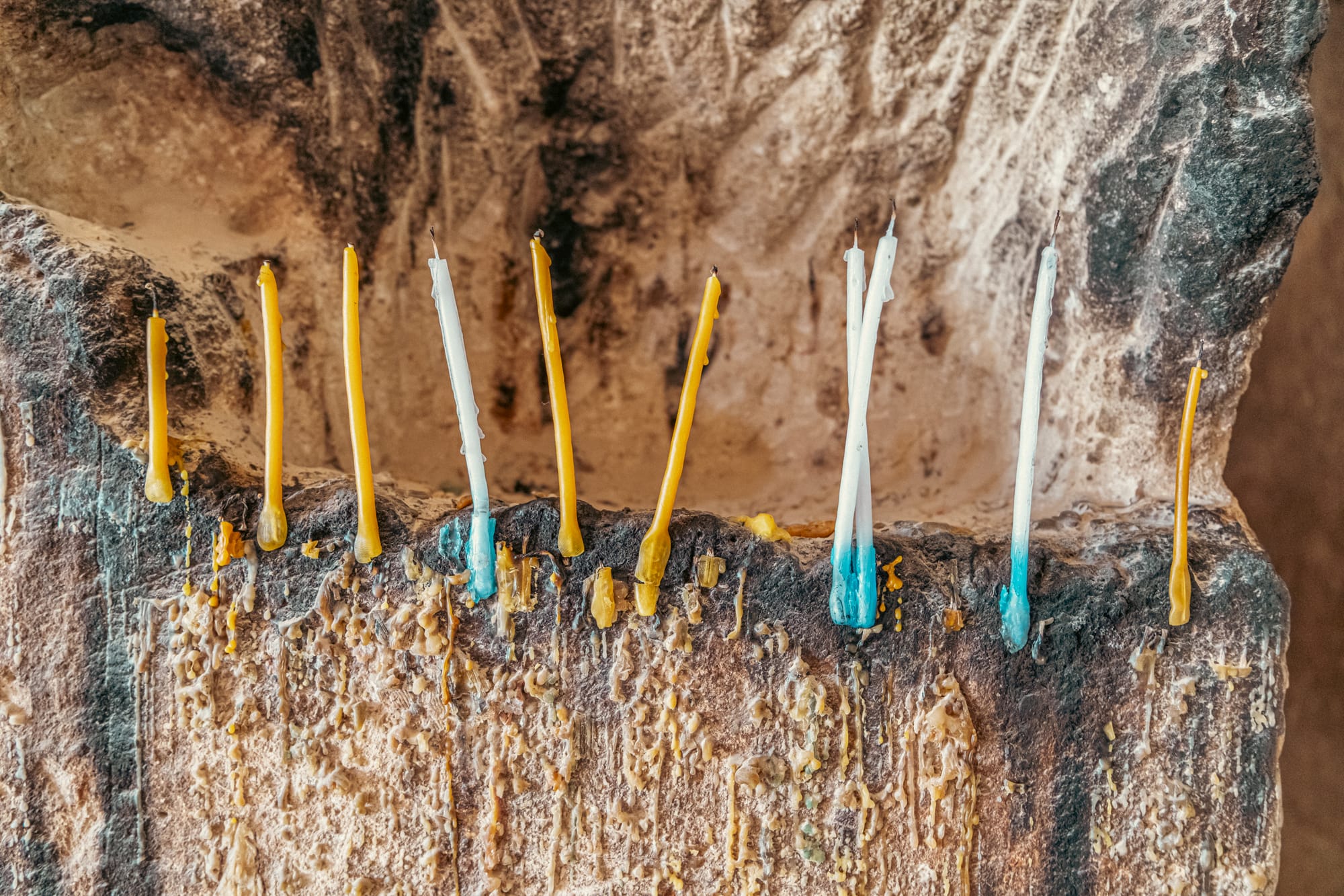 Close-up of colorful candles, yellow and blue-tipped white, placed in a stone crevice inside Çavuşin Castle