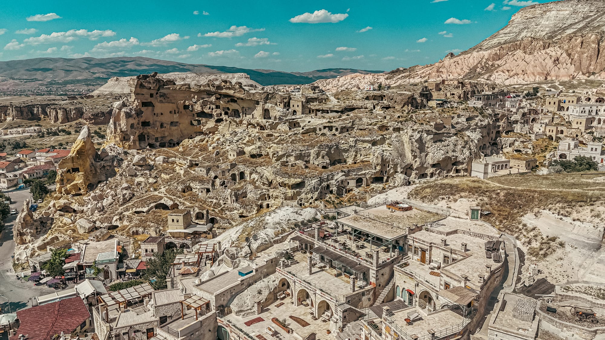 Aerial view of Çavuşin village in Cappadocia, showcasing its sprawling rock-cut dwellings, cave houses, and historic ruins set against surrounding mountains and valleys