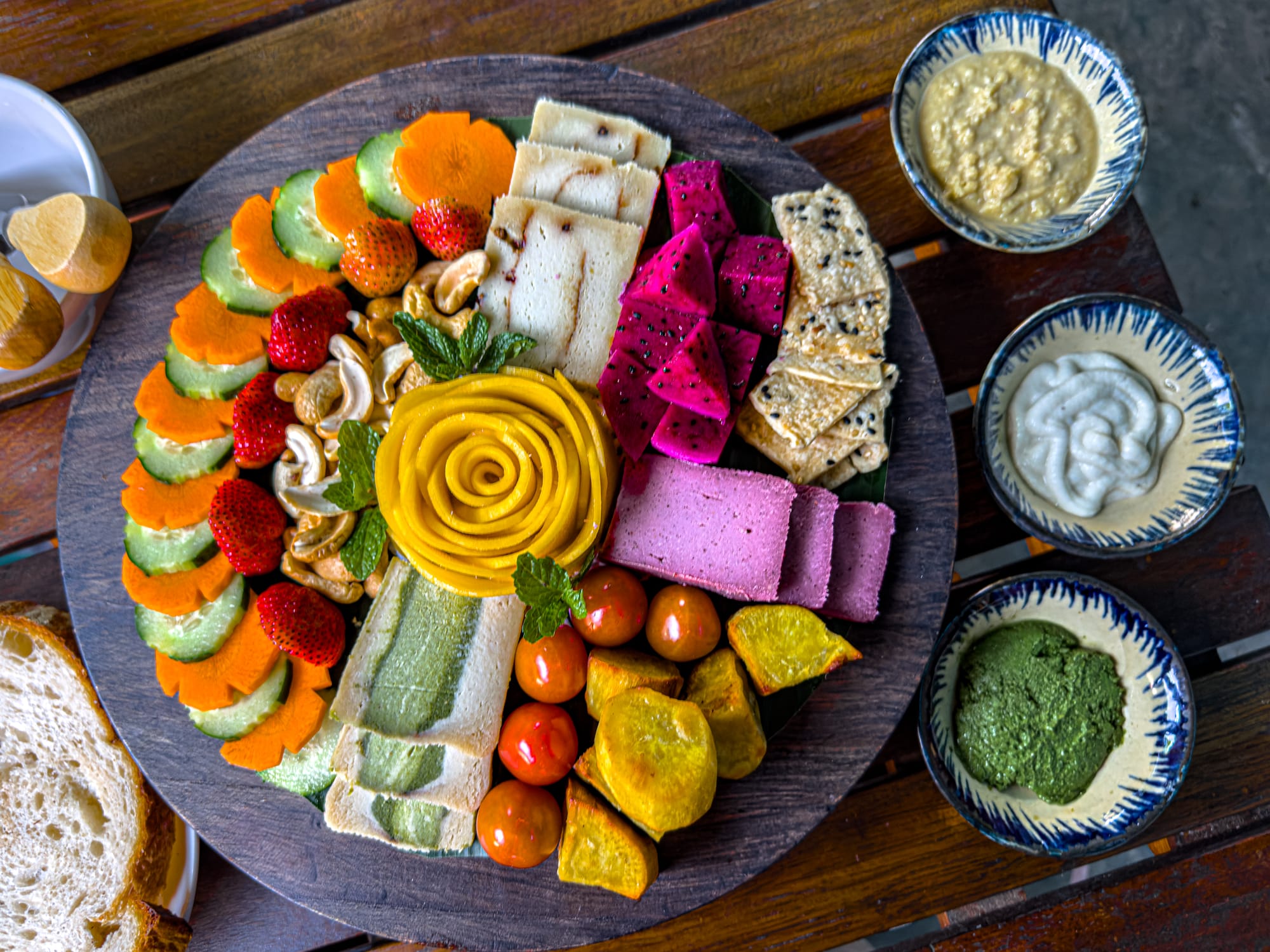 Vegan cheese and fruit platter at Chickpea Eatery in Hội An with cashews, strawberries, cucumber, carrot slices, dragon fruit, cherry tomatoes, sweet potato, crackers, and a carved mango rose centerpiece, served with three dipping sauces
